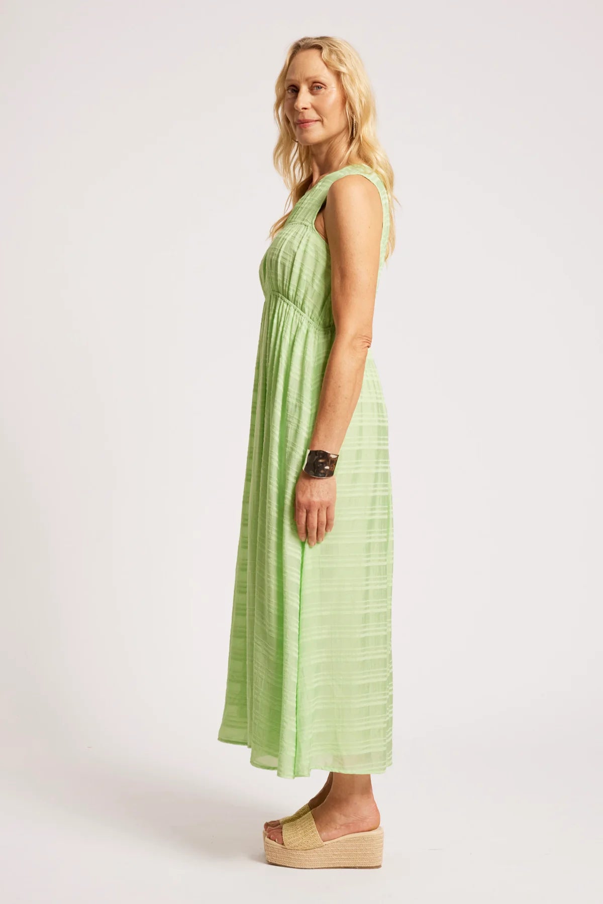 A woman modeling a Eb & Ive sleeveless light green maxi dress with a textured, pleated design, shown in profile against a plain light gray studio background.