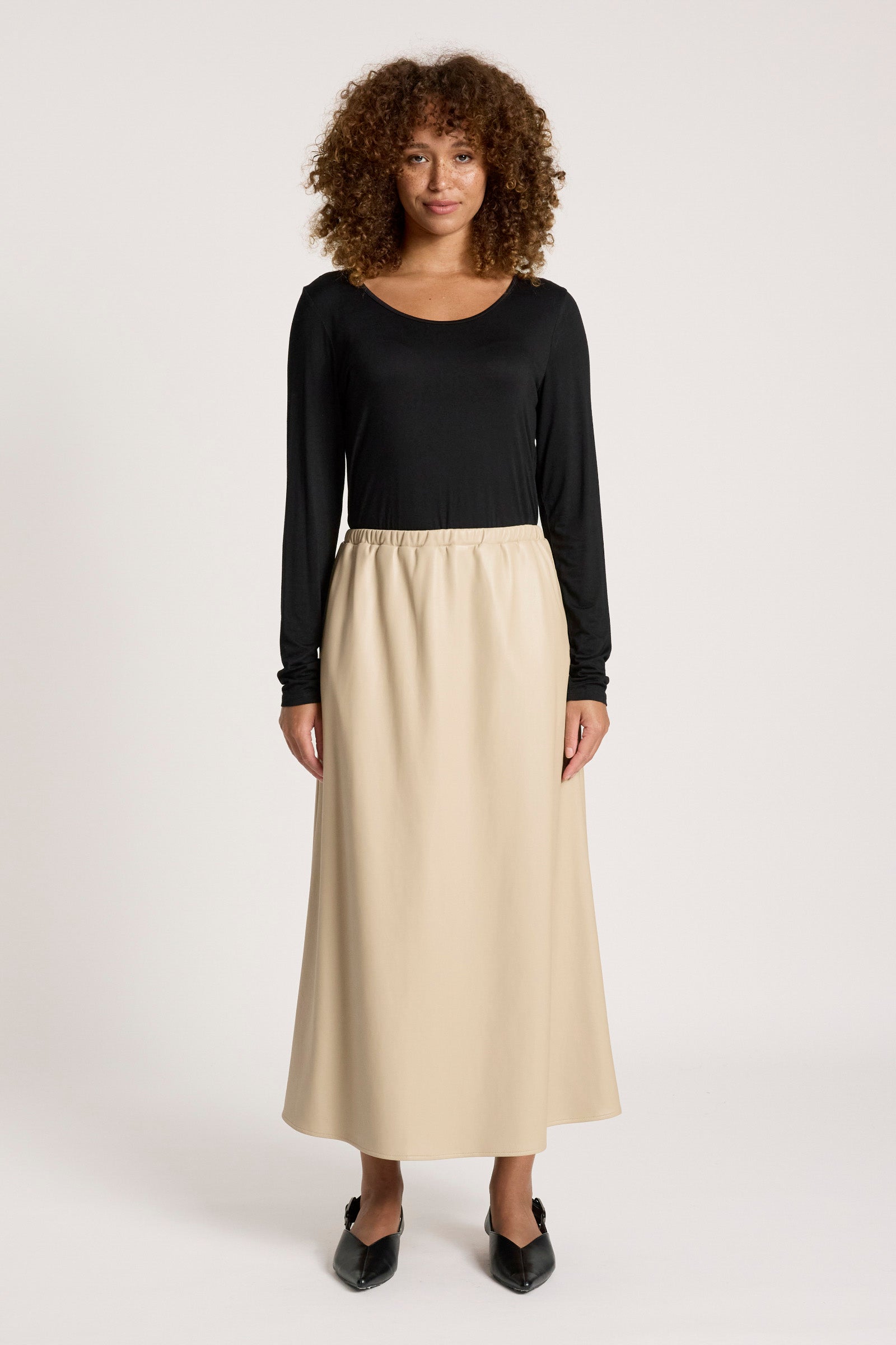 Image of Woman wearing a black top and Eb & Ive beige skirt on a white background