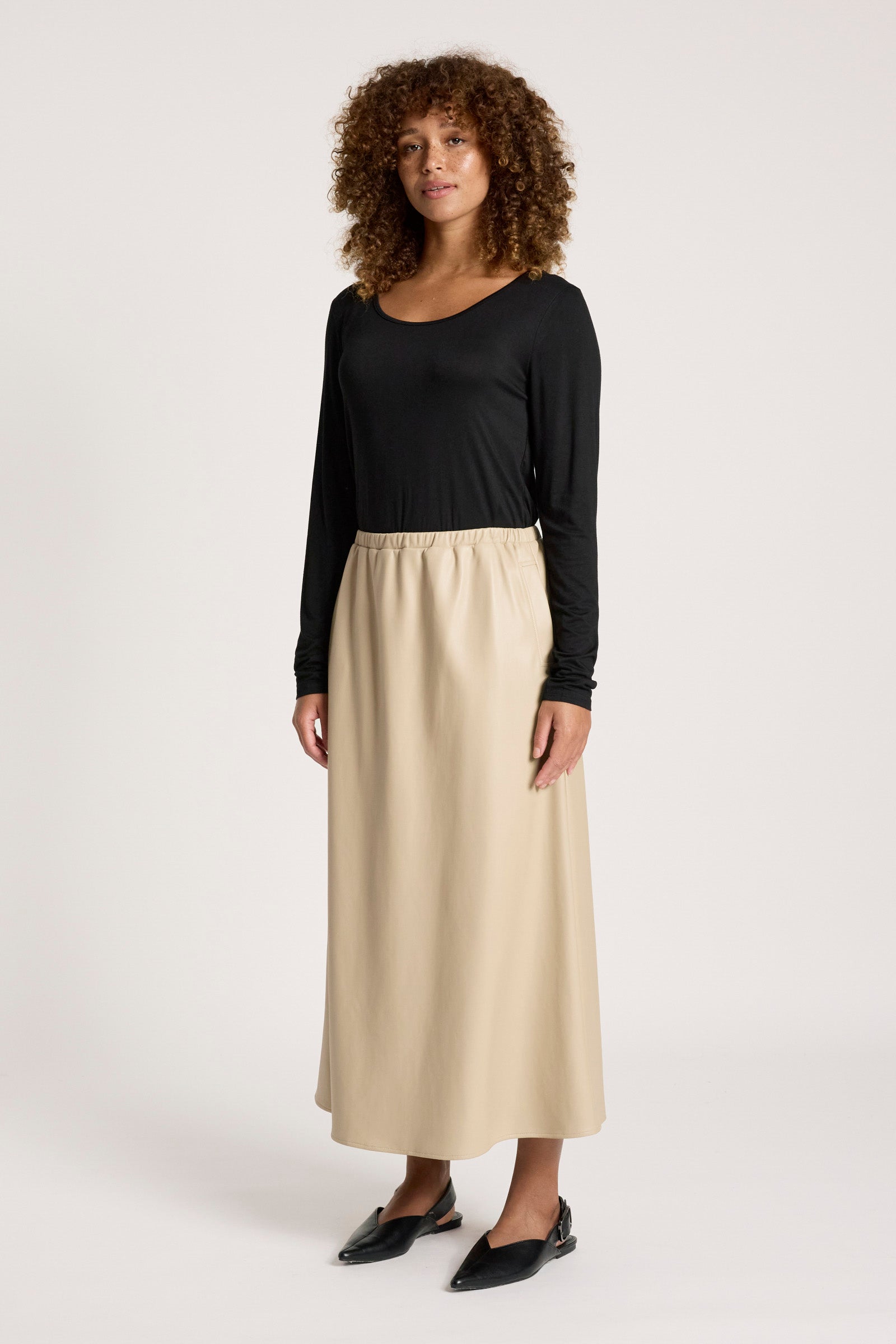 Image of Woman wearing a black top and Eb & Ive beige skirt on a white background