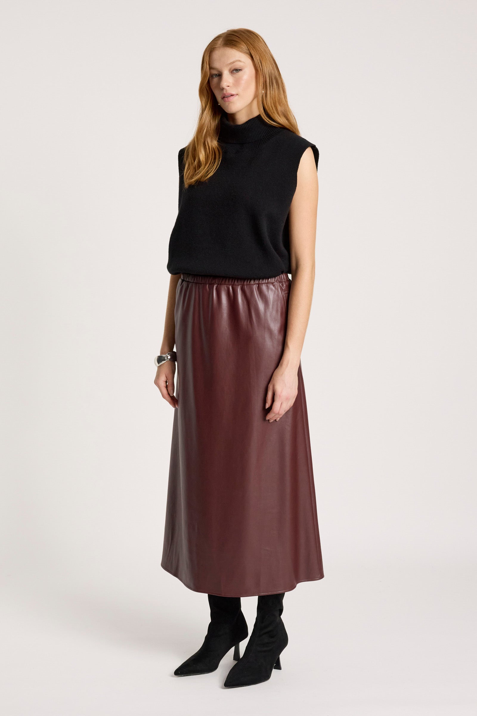 Woman wearing a black sleeveless top and Eb & Ive brown leather skirt on a white background