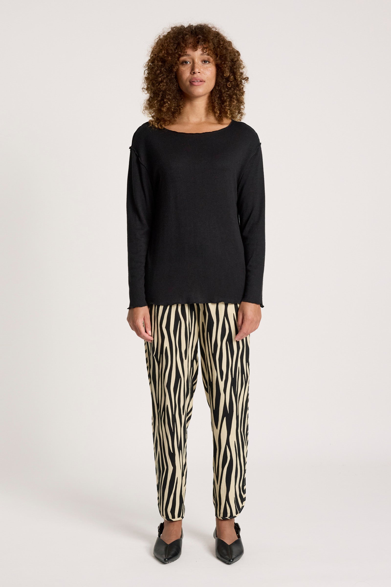 Woman wearing a Eb & Ive black top and zebra print pants on a white background