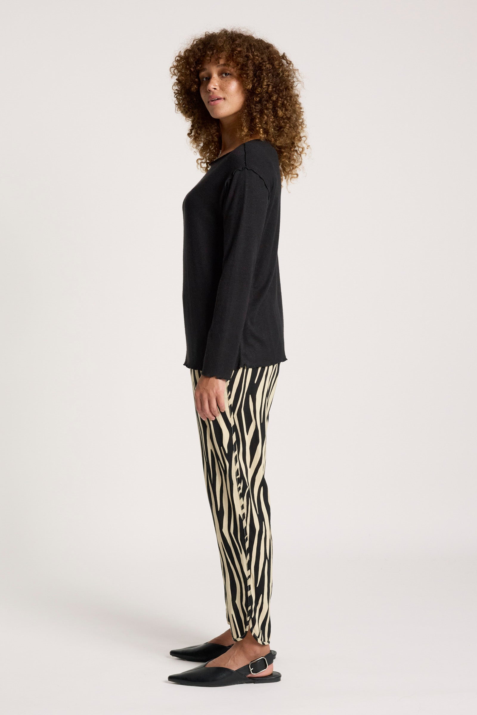 Woman wearing a Eb & Ive black top and zebra print pants on a white background