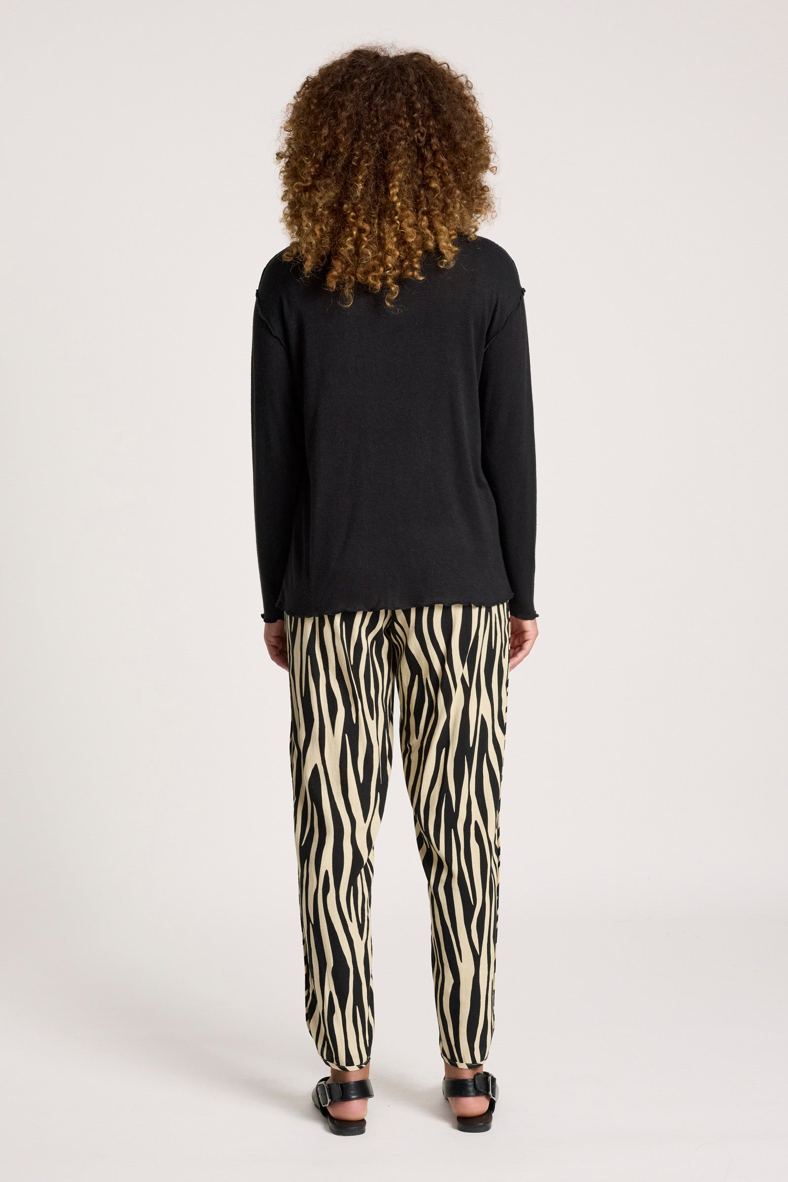 Woman wearing a Eb & Ive black top and zebra print pants on a white background