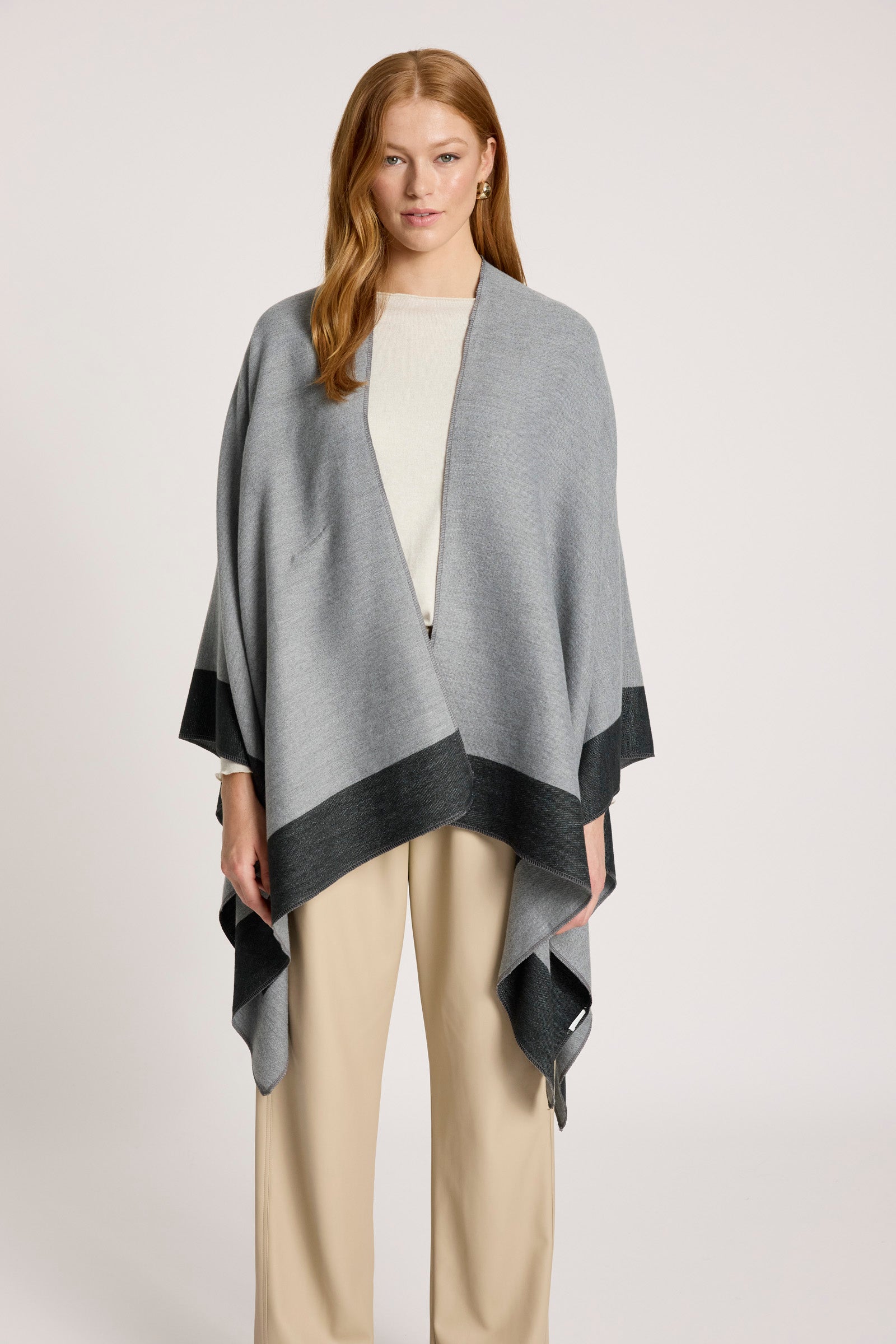 Image of Woman wearing a Eb and Ive gray and black shawl over a white top and beige pants on a light background