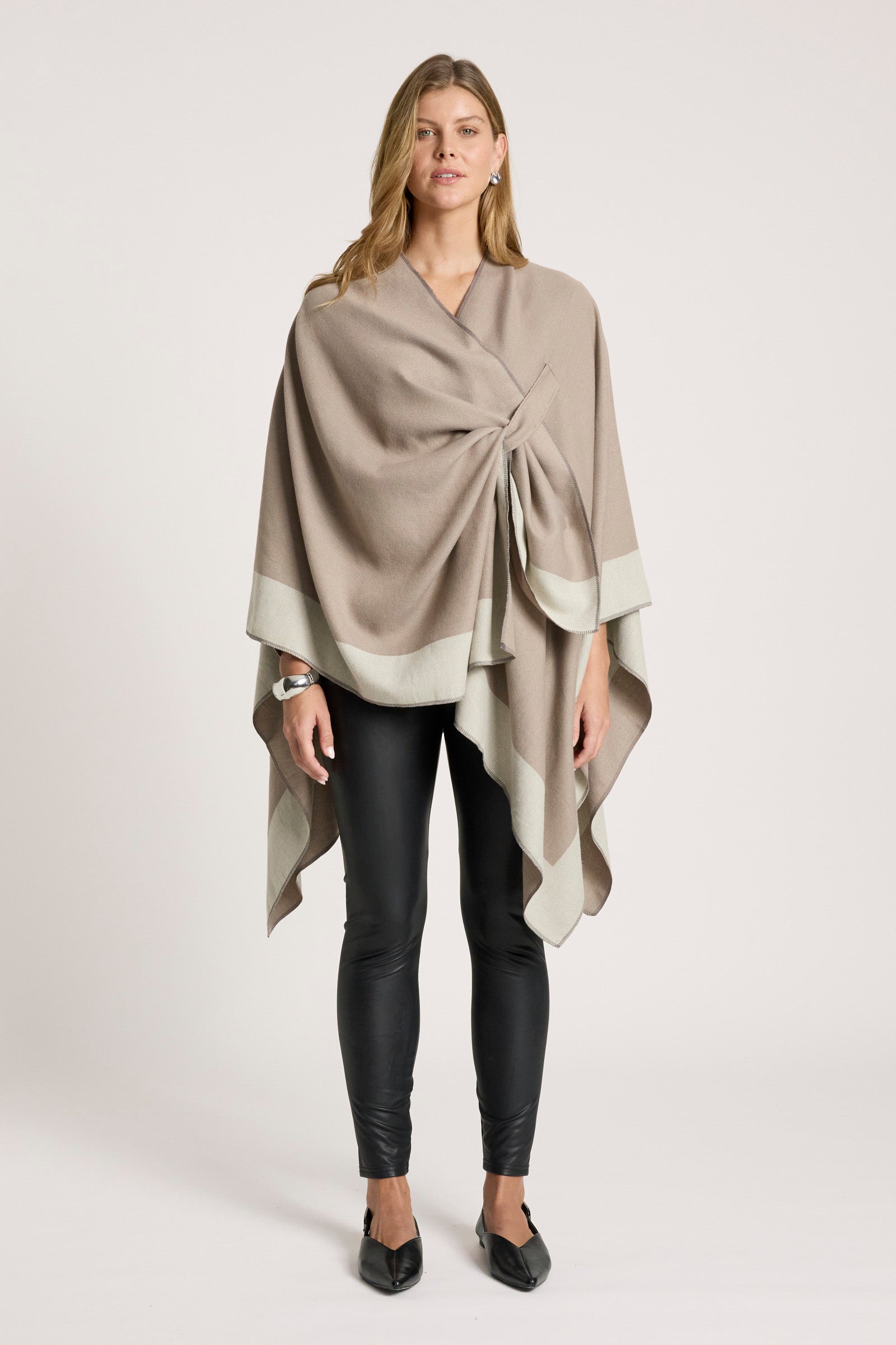Woman wearing a Eb & Ive beige wrap over a neutral top and black pants on a white background