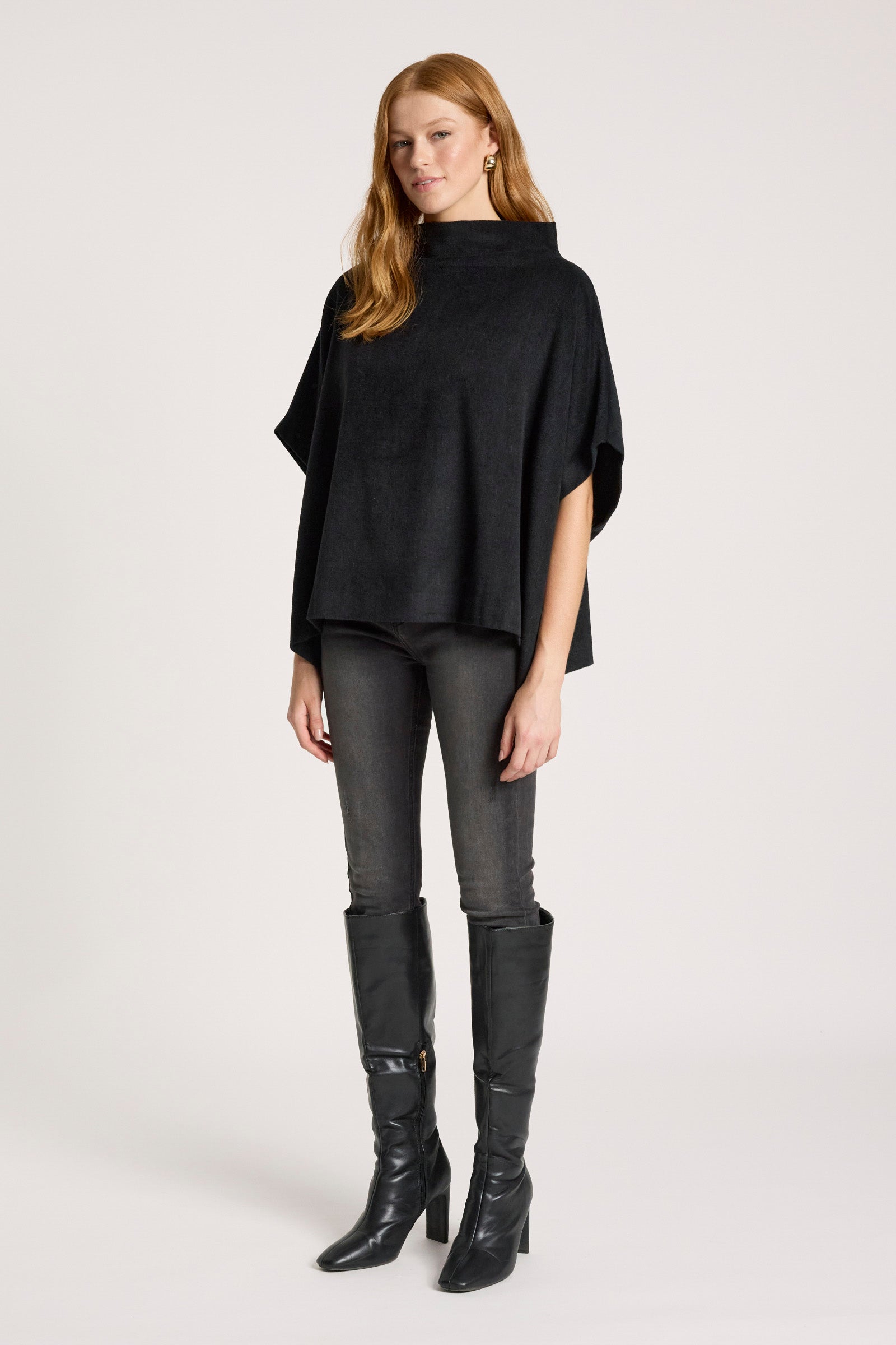 Image of Woman wearing a Eb and Ive black poncho, leggings, and high boots on a white background