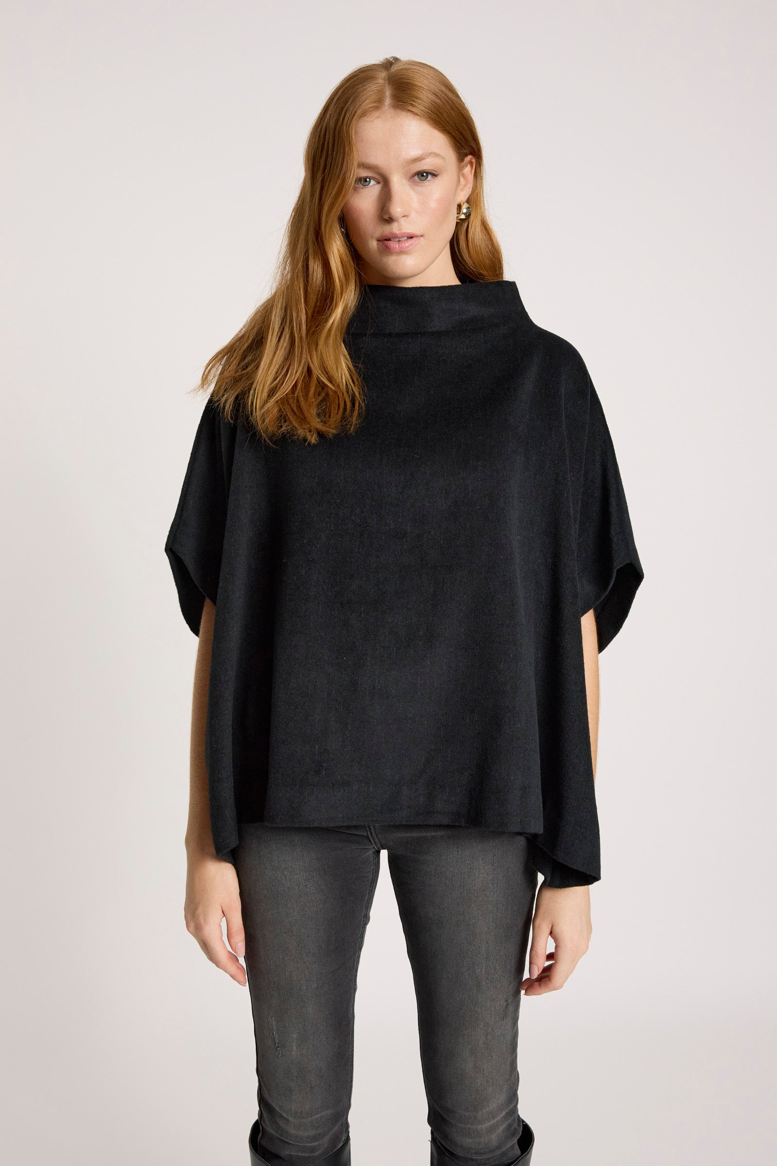 Image of Woman wearing a Eb & Ive black poncho and dark pants on a white background