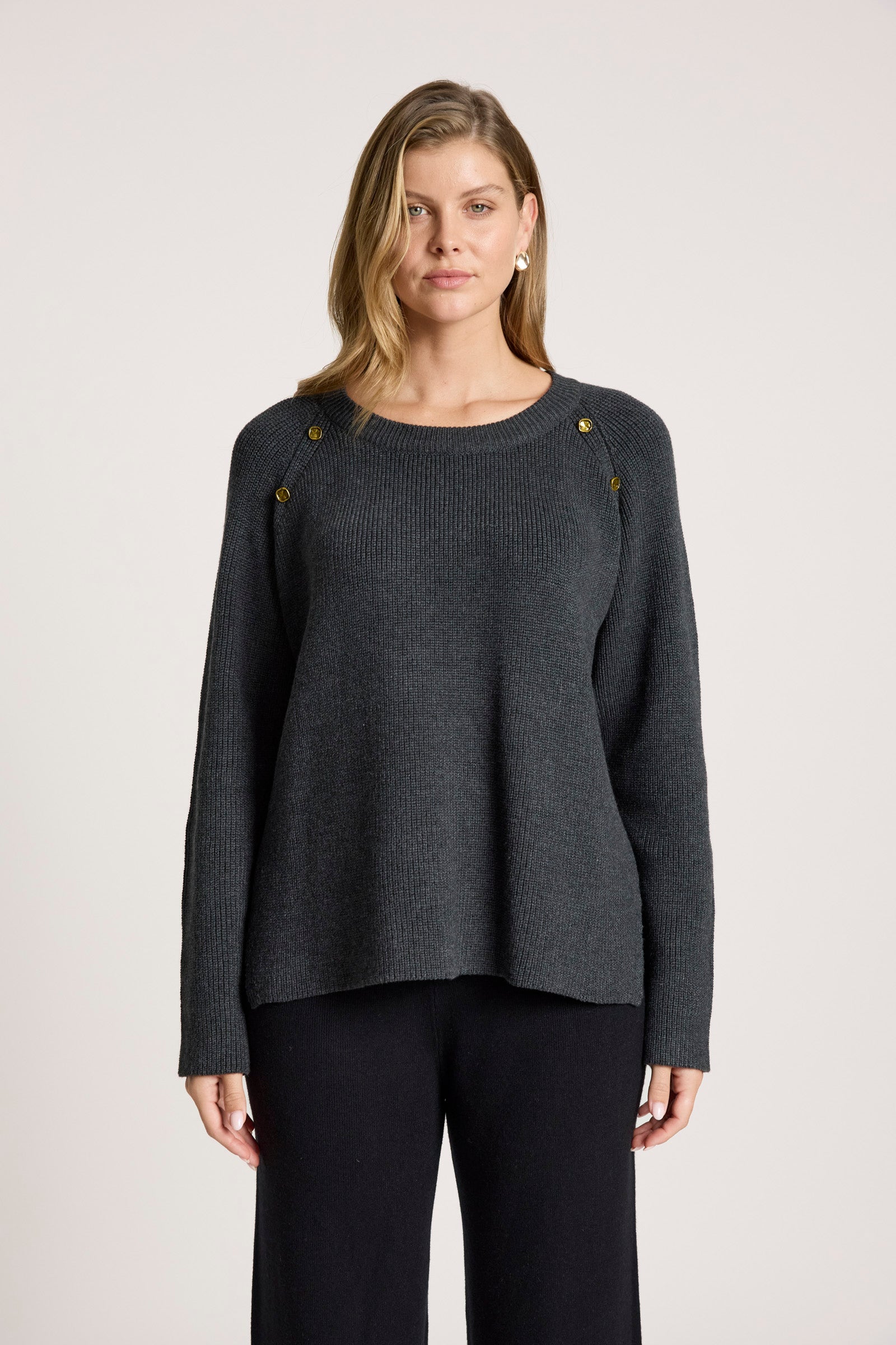 Image of Woman wearing a Eb & Ive dark grey sweater with gold buttons on a light background