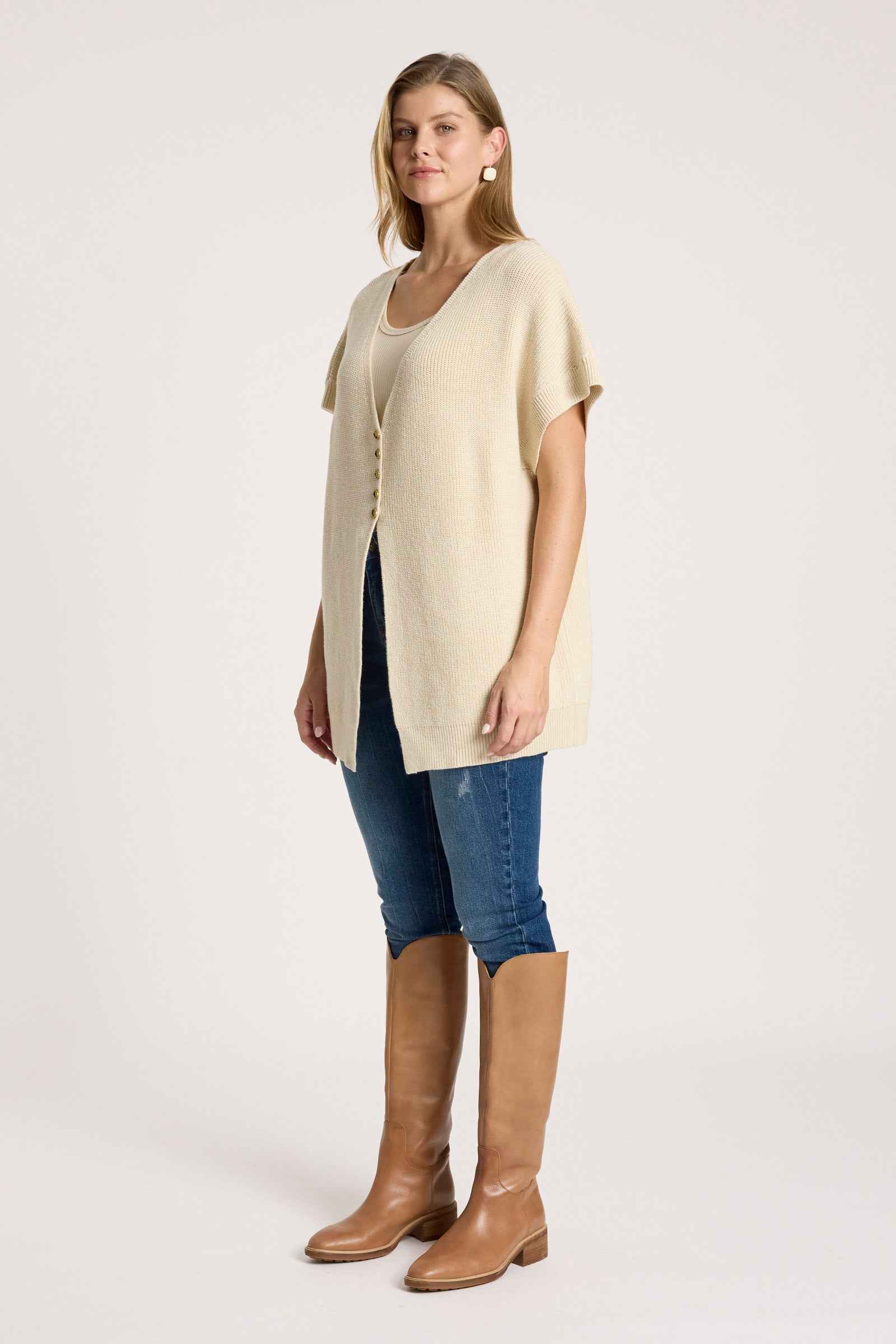 Woman wearing a Eb & Ive beige cardigan, blue jeans, and brown knee-high boots on a white background