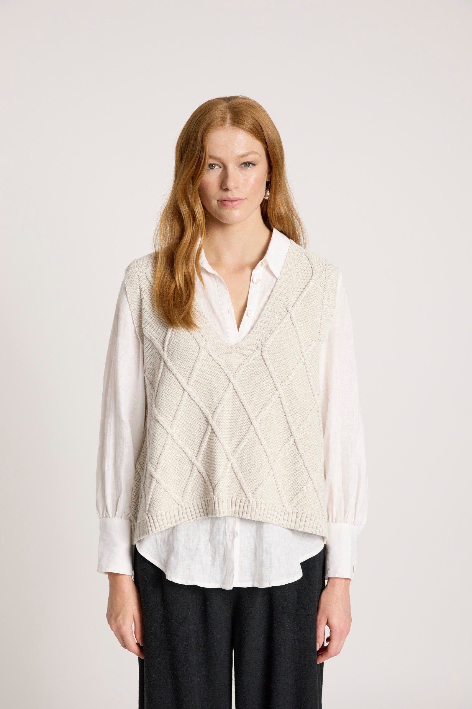 Image of Woman wearing a Eb and Ive cream sweater vest over a white shirt on a plain background
