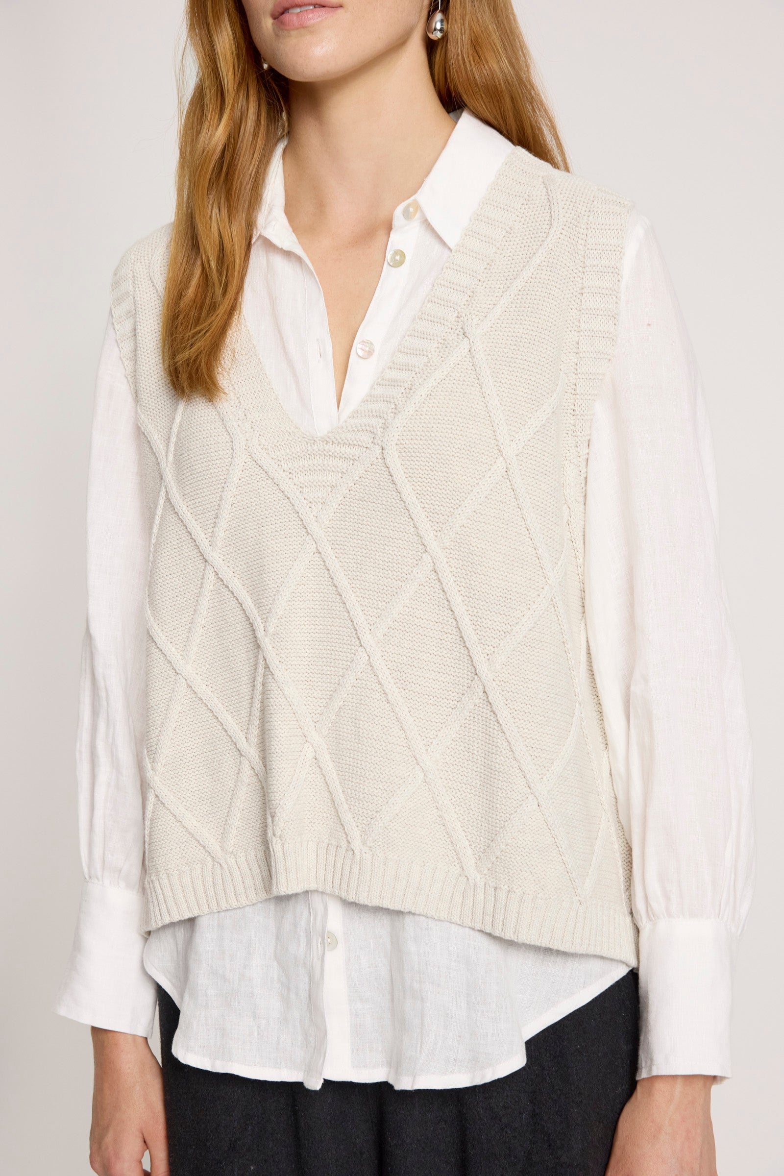 Image of Woman wearing a Eb and Ive cream-colored cable knit vest over a white shirt with a plain background