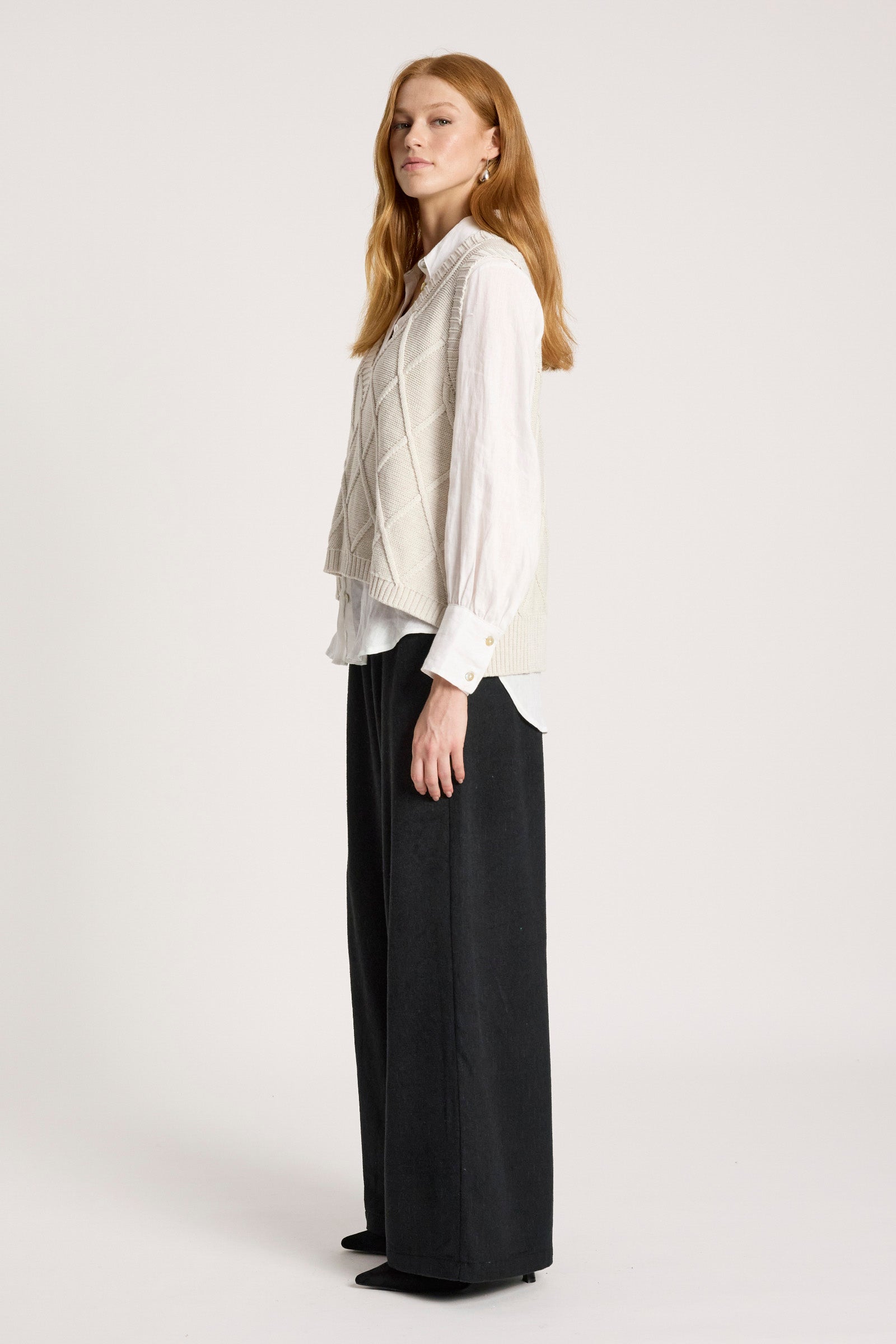 Woman wearing a Eb and Ive white blouse with a patterned vest and black pants on a white background