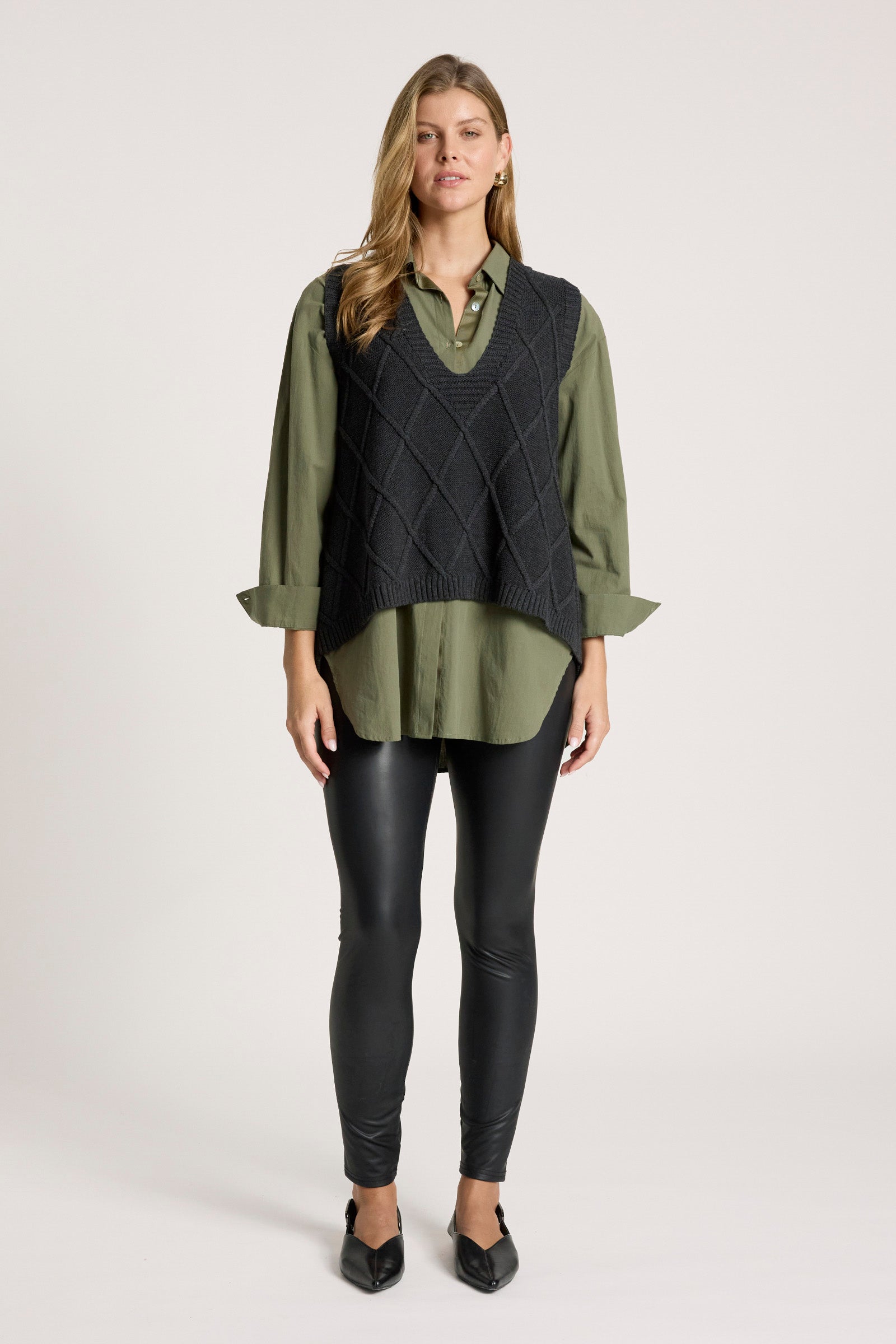 Image of Woman wearing a dark green shirt with a Eb and Ive black knitted vest on a white background