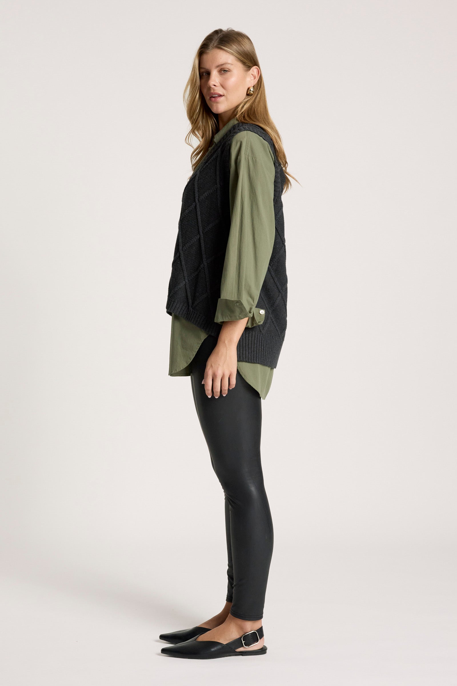 Image of Woman wearing a dark green shirt with a Eb and Ive black knitted vest on a white background