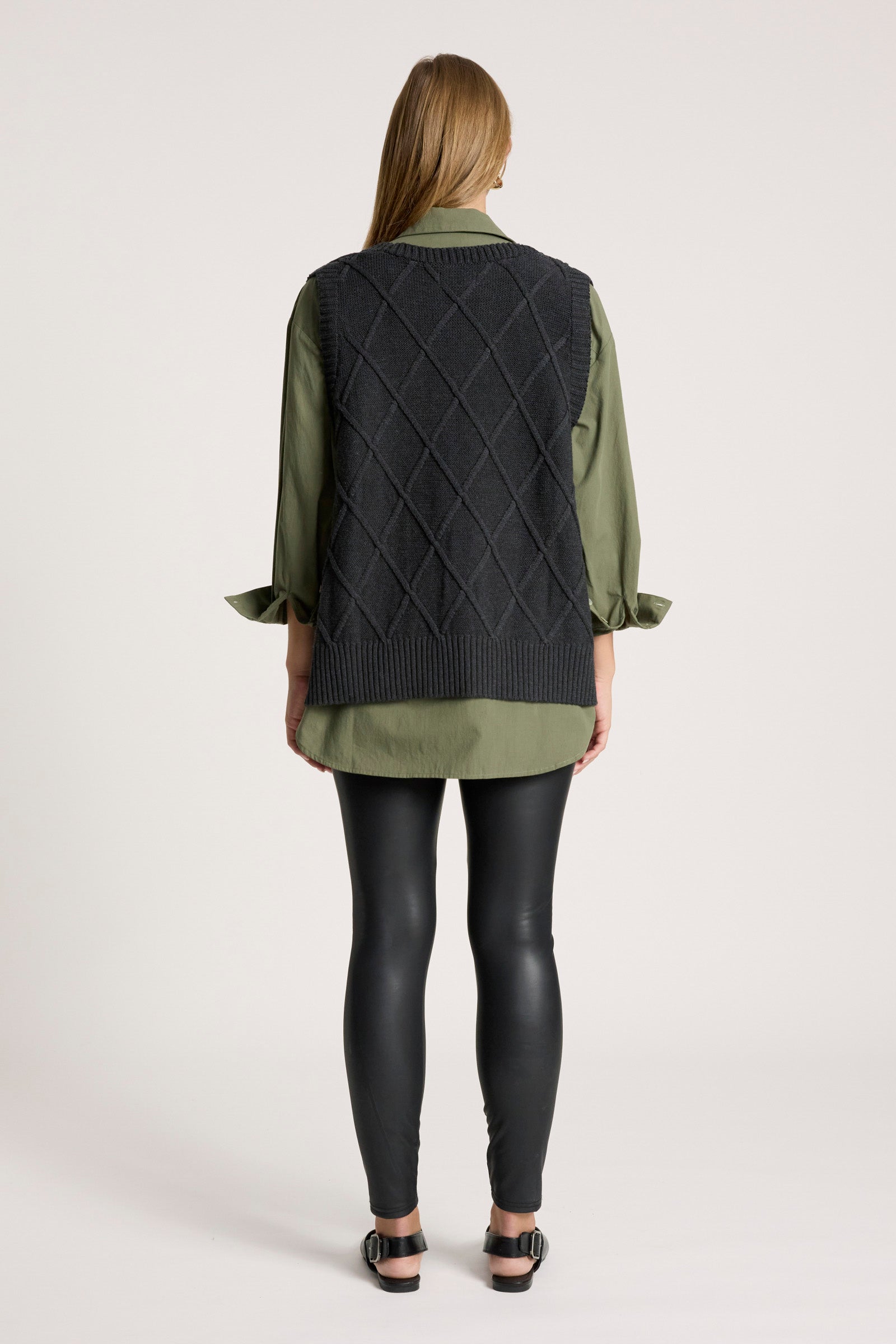Image of Person wearing a green sweater with a Eb and Ive black quilted vest over it on a white background