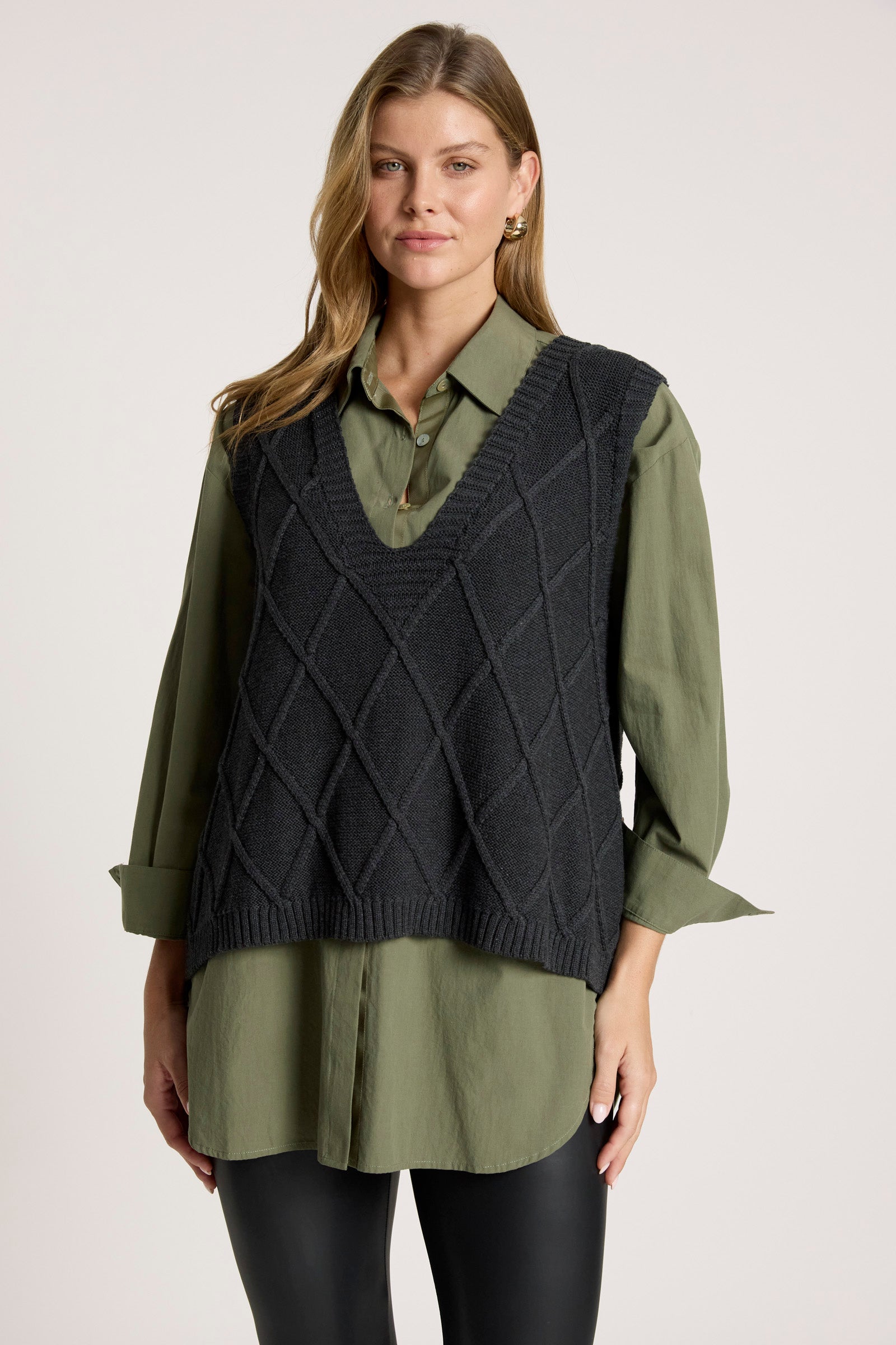 Image of Woman wearing a dark green shirt with a Eb and Ive black knitted vest on a white background