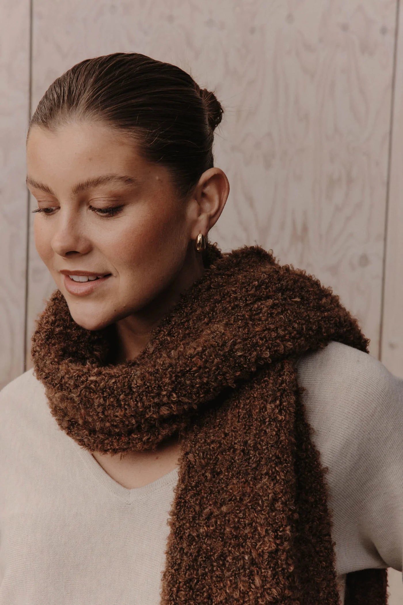 Image of Woman wearing a Eb & Ive brown knitted scarf against a wooden background