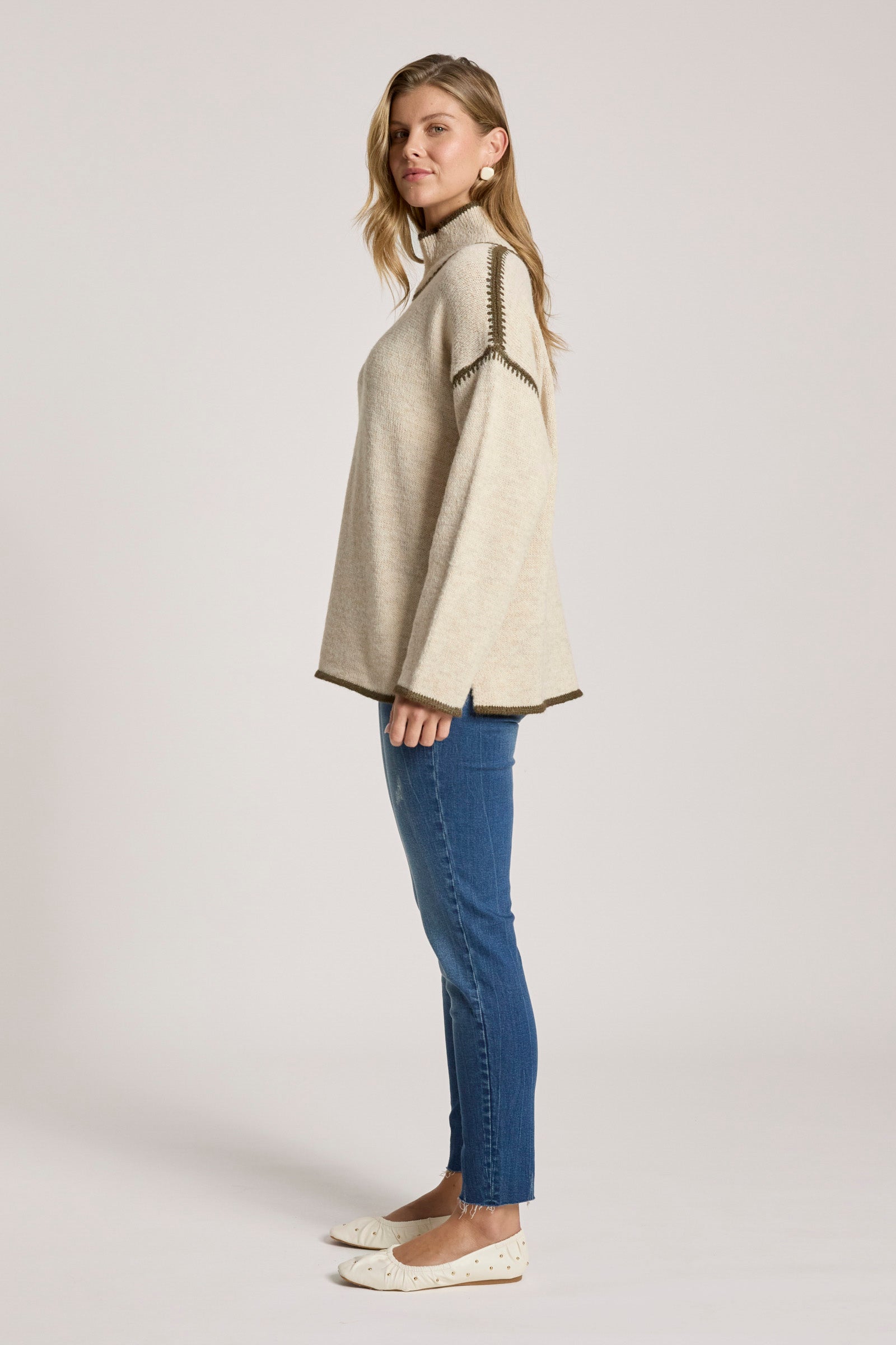 Image of Woman wearing a Eb & Ive beige poncho and blue jeans on a plain background