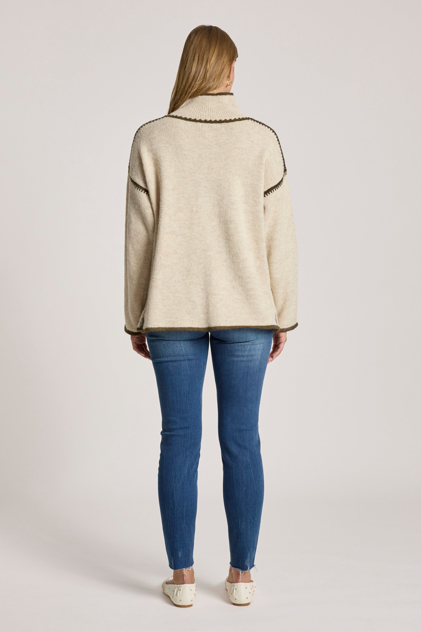 Woman wearing a Eb & Ive beige jacket and blue jeans on a plain background