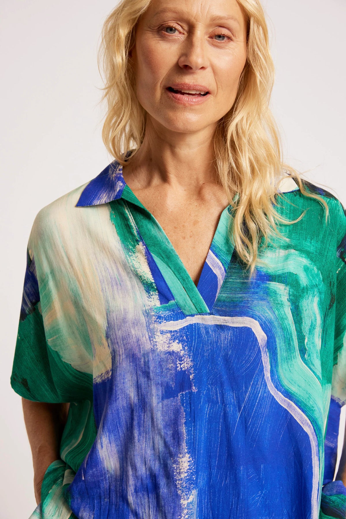 A close-up of a woman wearing a Eb & Ive short-sleeve V-neck blouse with an abstract painterly print in shades of blue, green, and cream.