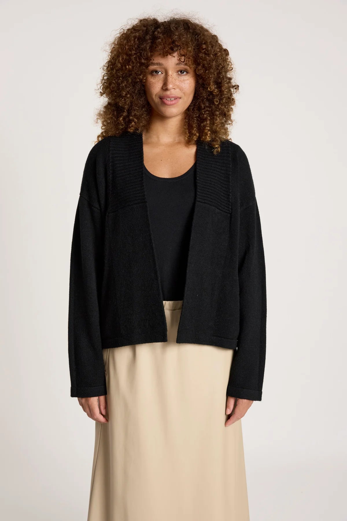 Image of Woman wearing a Eb & Ive black jacket over a black top and beige pants on a plain background