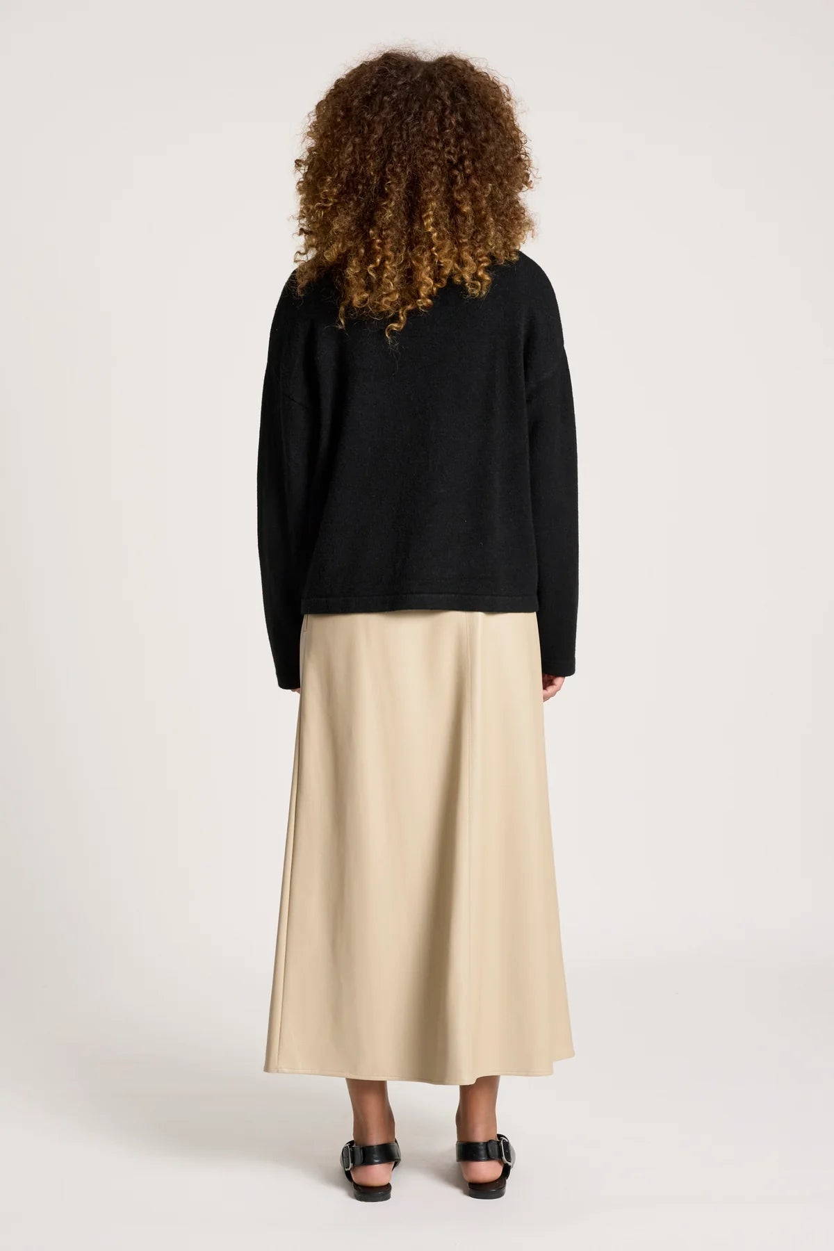 Image of Woman wearing a black cardigan and beige skirt on a white background
