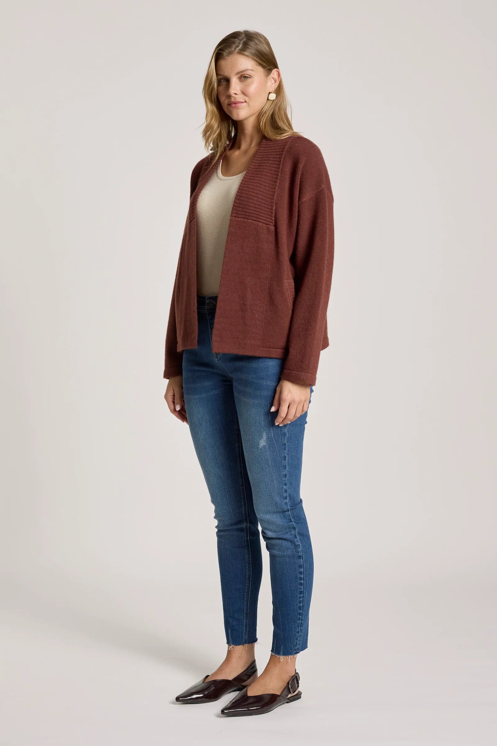 Image of Woman wearing a Eb & Ive brown jacket, beige top, blue jeans, and black flats on a white background