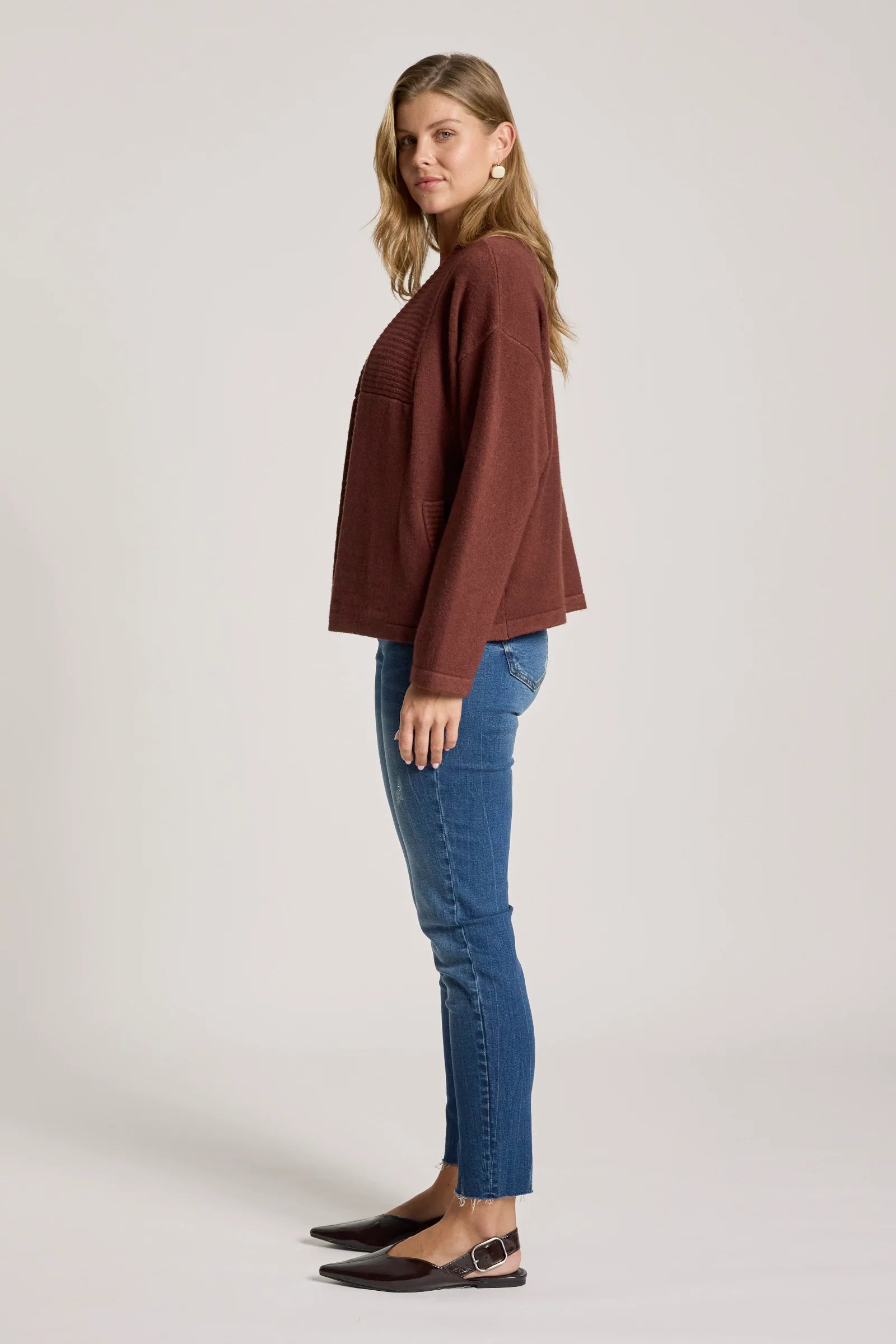Woman wearing a Eb & Ive brown top and blue jeans on a light gray background