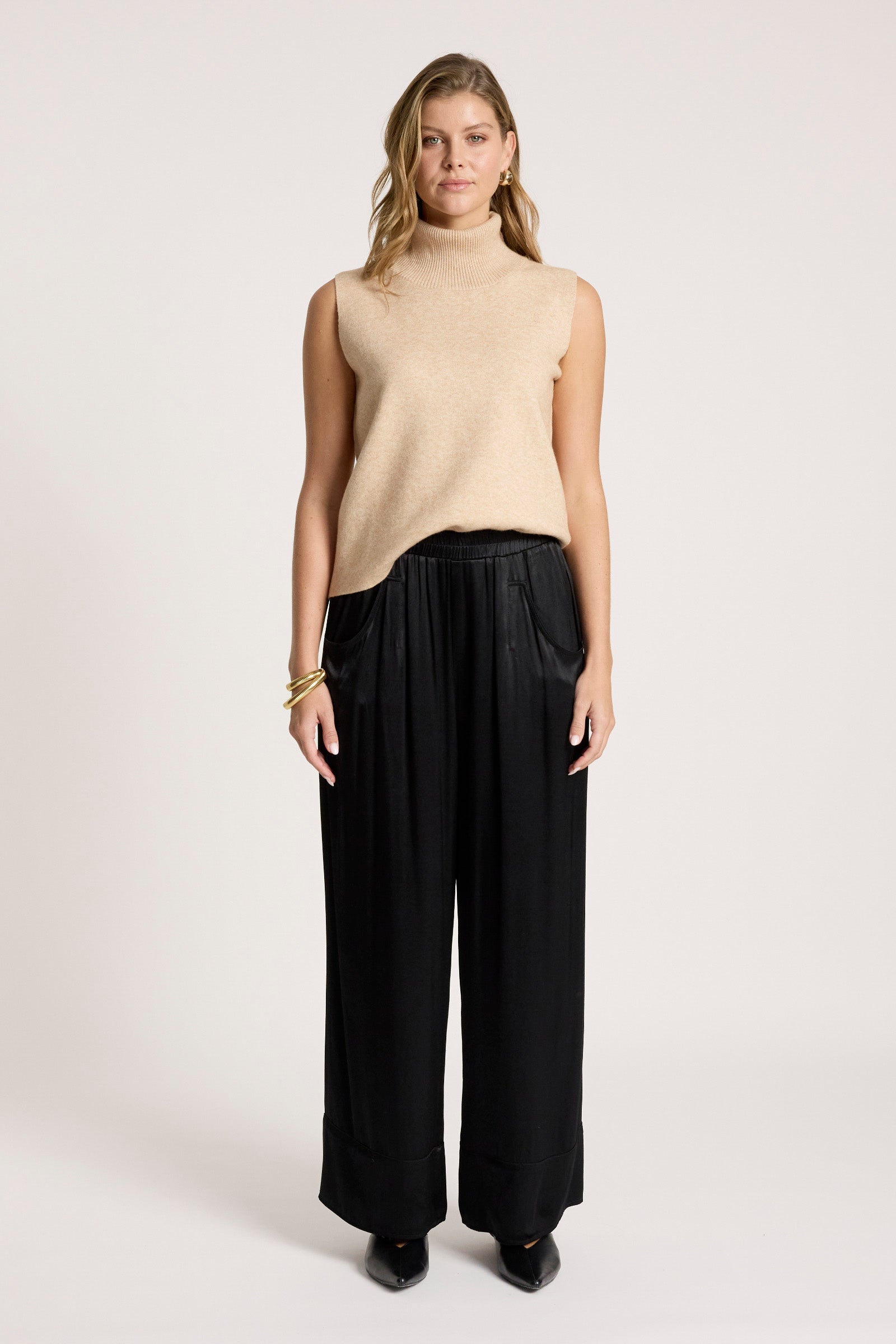 Image of Woman wearing a beige sleeveless sweater and Eb & Ive black pants on a white background
