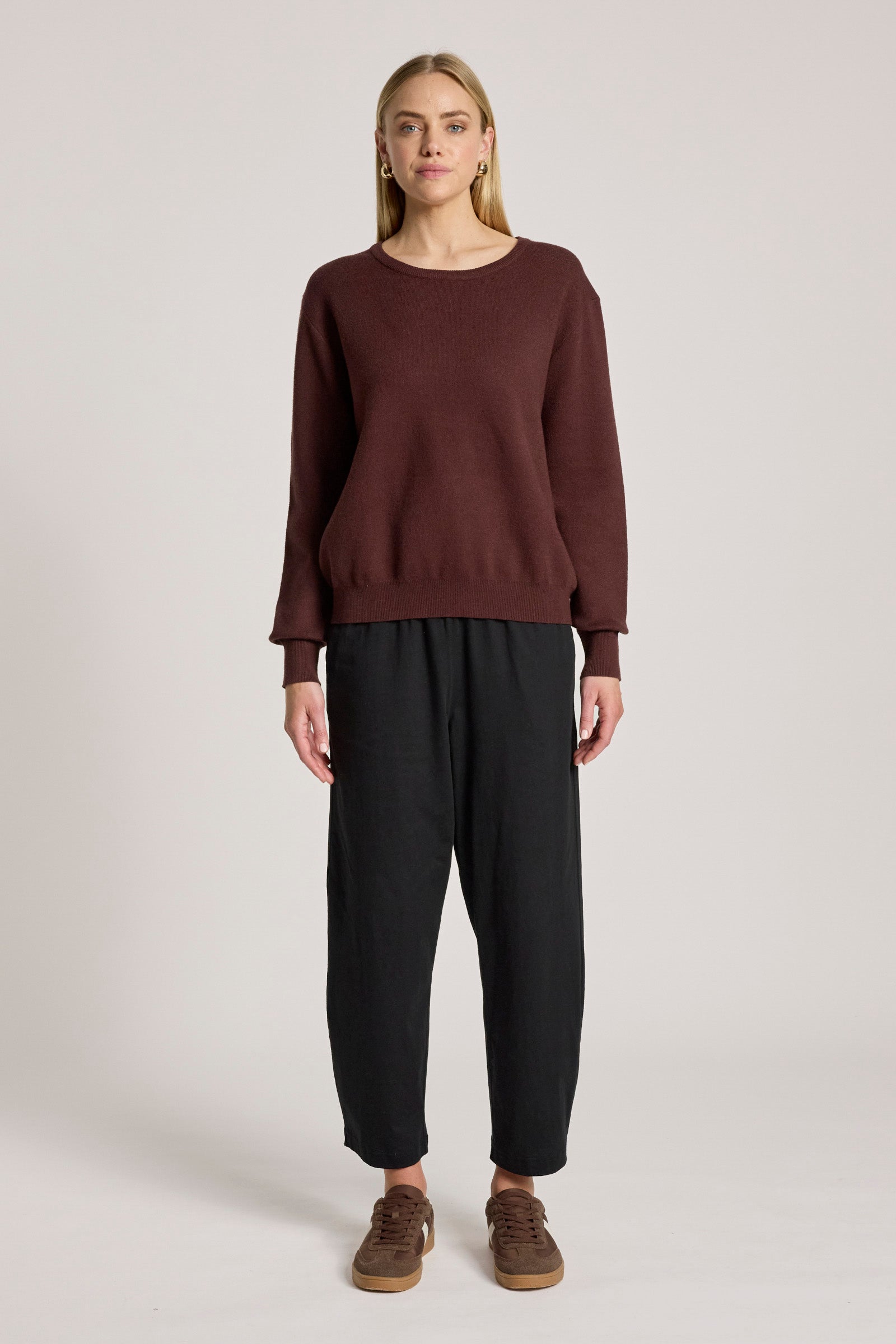 Woman wearing a Eb & Ive brown sweater and black pants on a light gray background