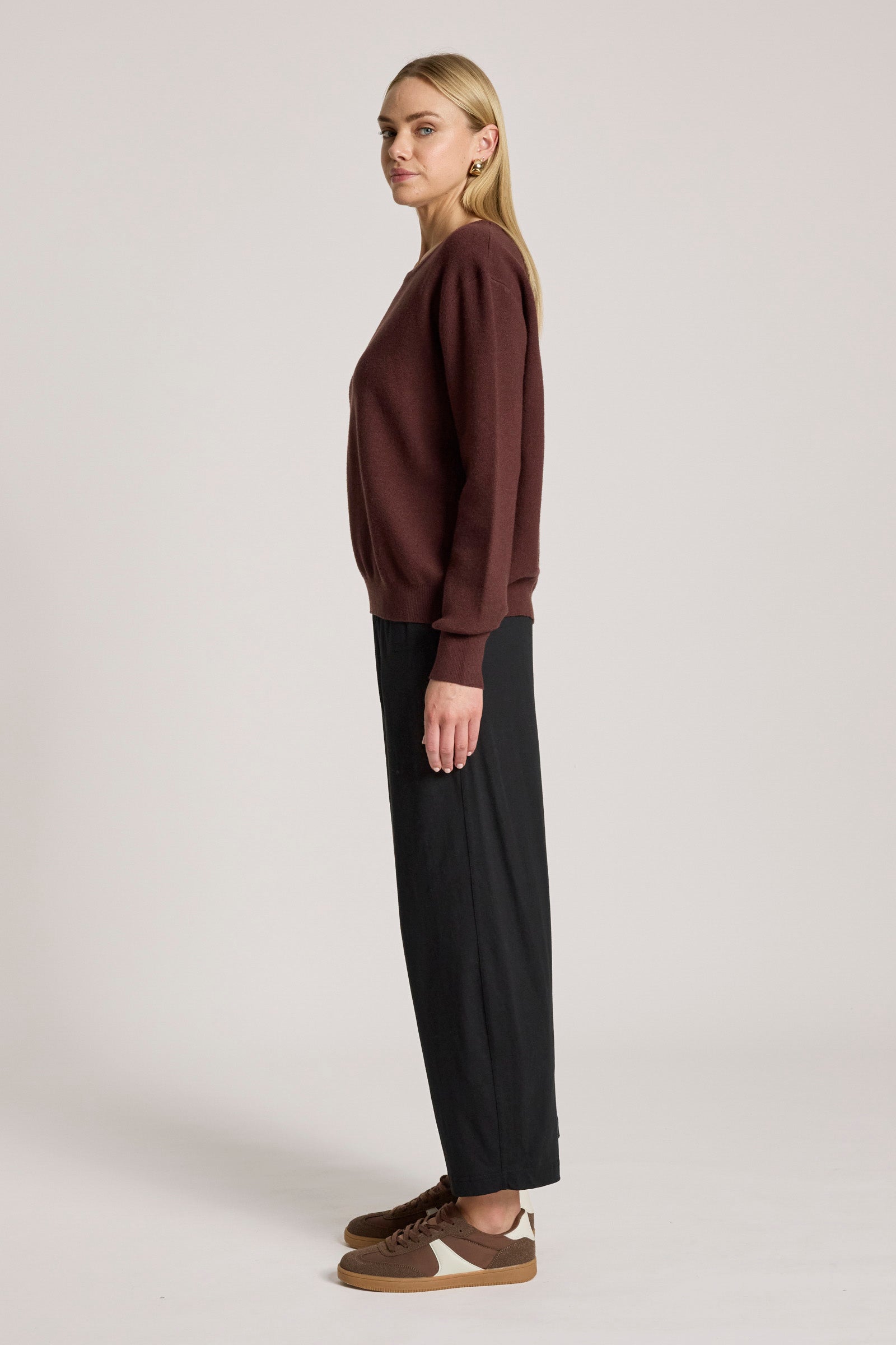Woman wearing a Eb & Ive brown sweater and black pants on a light gray background