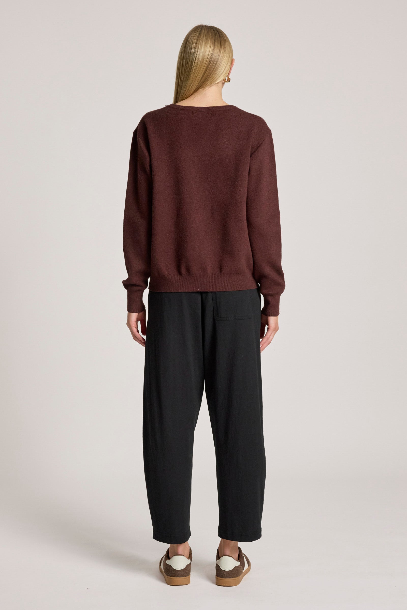 Woman wearing a Eb & Ive brown sweater and black pants on a light gray background