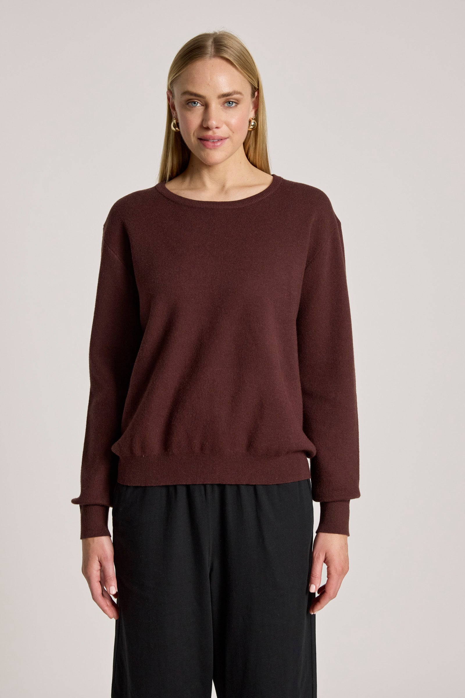 Image of Woman wearing a Eb & Ive brown sweater and black pants on a light gray background