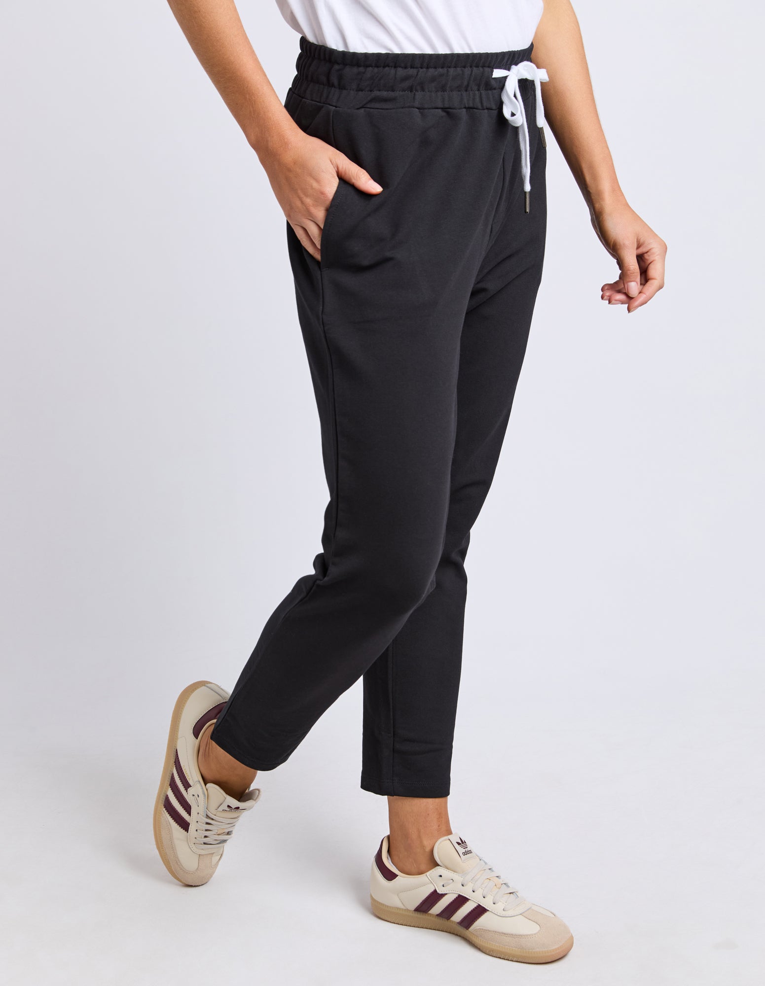 Image of Sideview of a woman wearing Elm black track pants with a white background