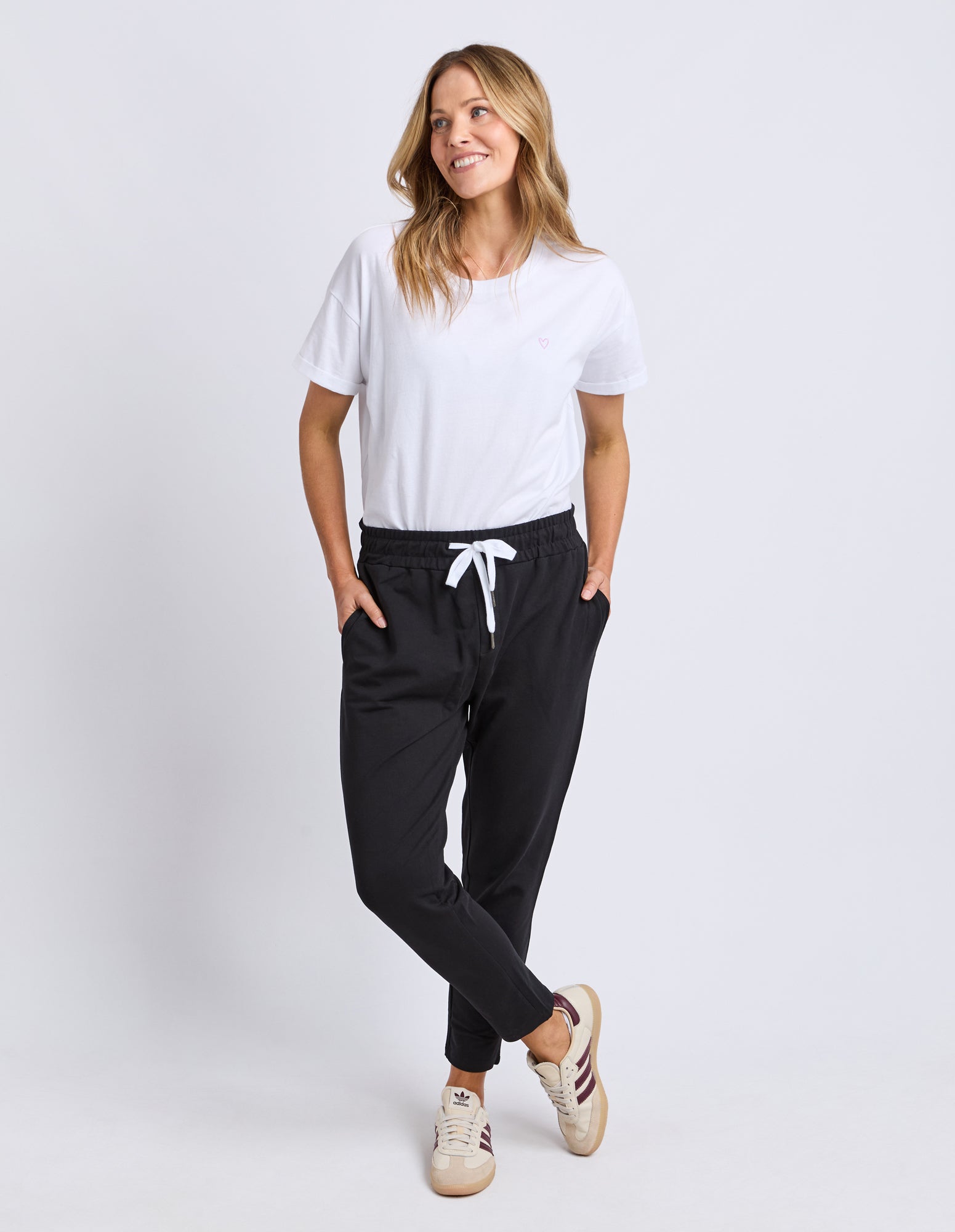Image of Woman wearing a white t-shirt and Elm black track pants with a white drawstring on a light grey background