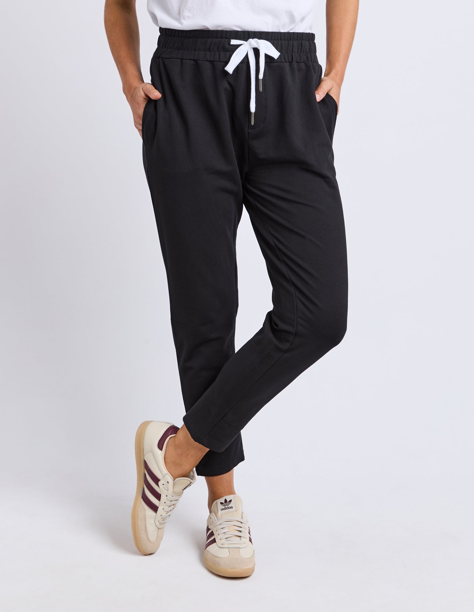 Image of Woman wearing Elm black track pants with white drawstring and beige sneakers on a light grey background