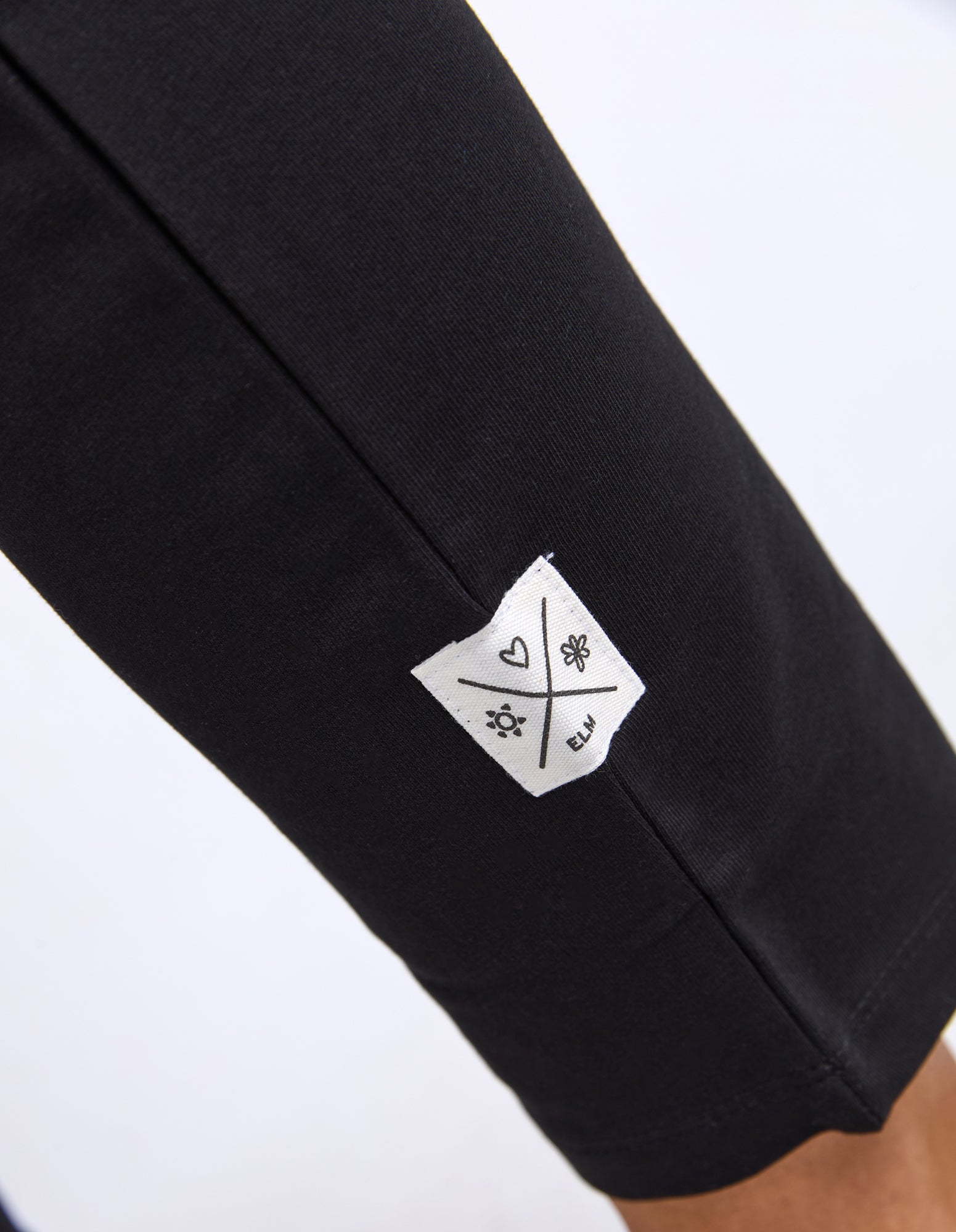 Black track pant with a white label featuring Elm symbols on a white background