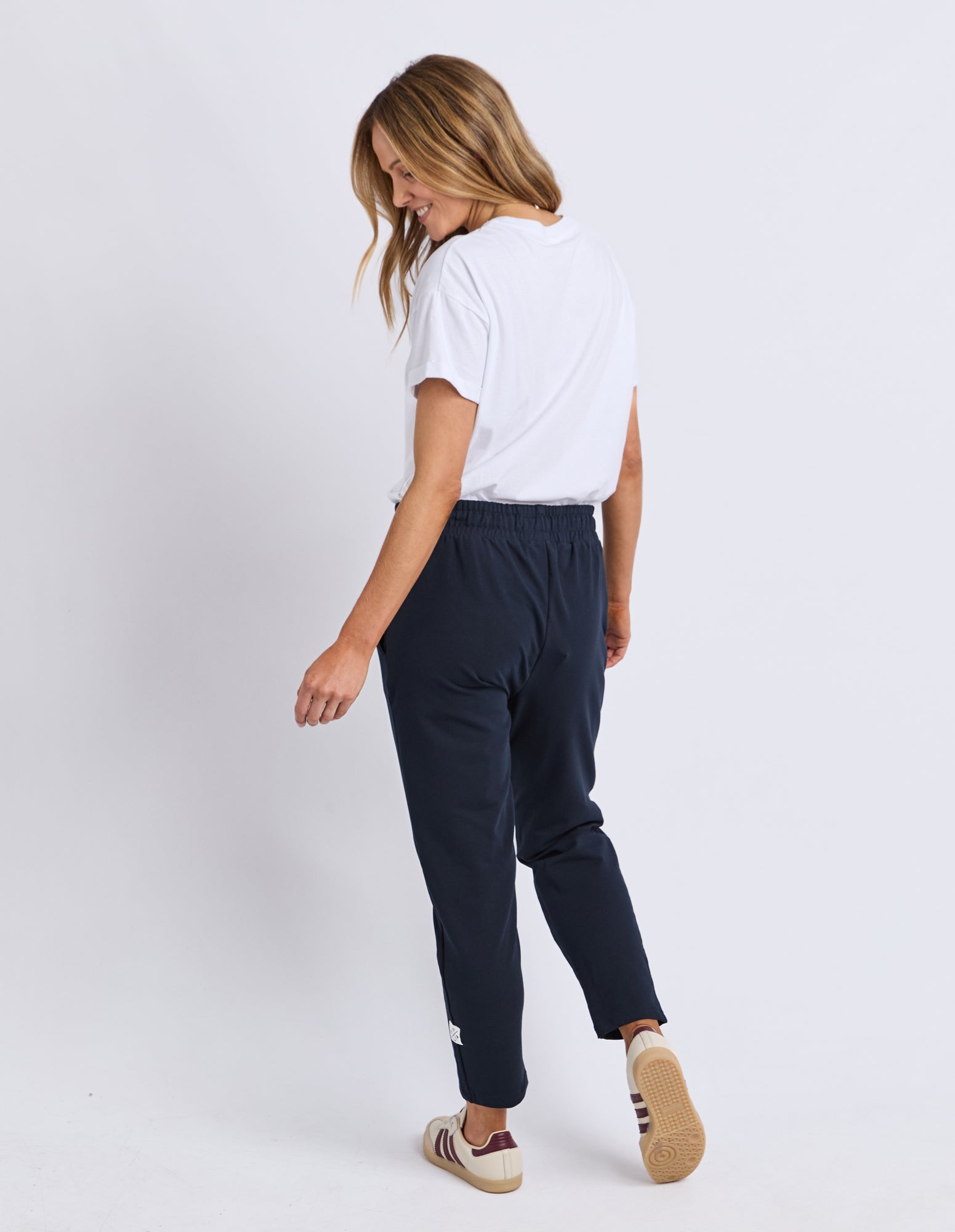 Image of Back view of a woman wearing Elm navy track pants and a white t-shirt on a white background