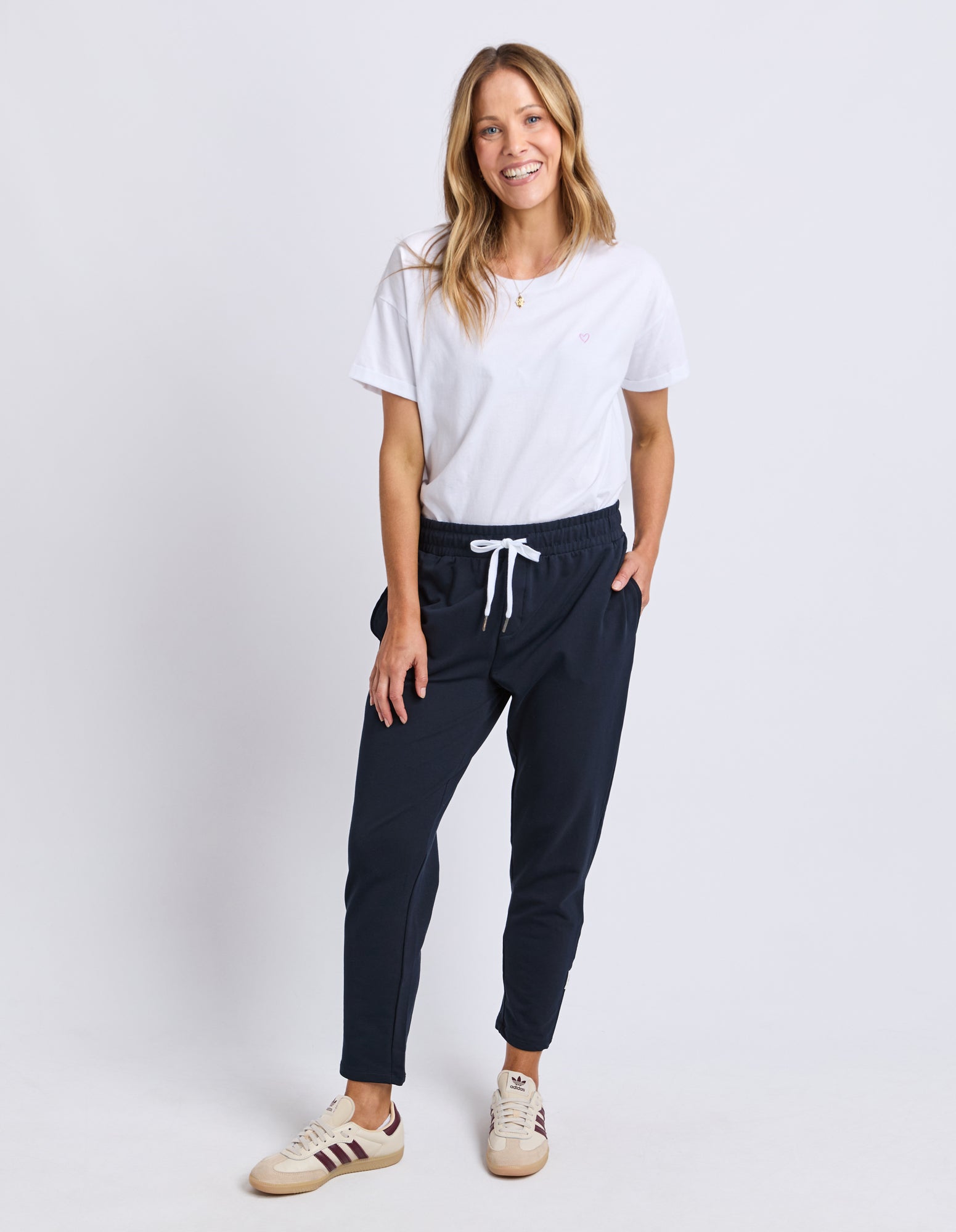 Image of Woman wearing a white t-shirt and Elm navy track pants on a white background
