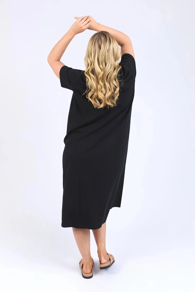 Image of A woman modeling a Elm loose-fitting black short-sleeve midi dress with an asymmetrical draped hem, styled with tortoiseshell sunglasses and brown strappy sandals against a plain white studio background.