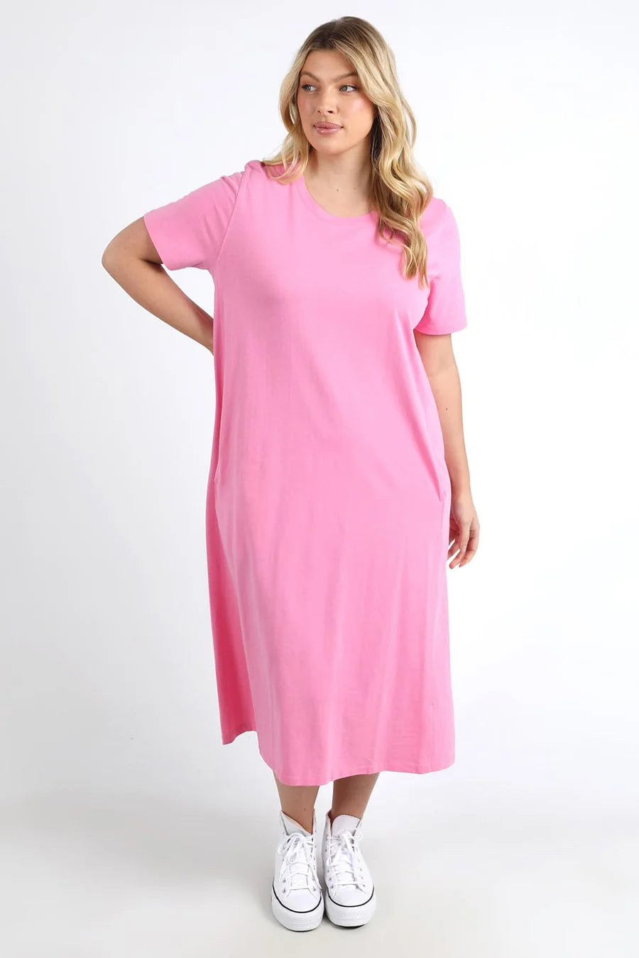 A woman modeling a Elm bright pink short-sleeve midi dress with white sneakers against a plain white studio background.