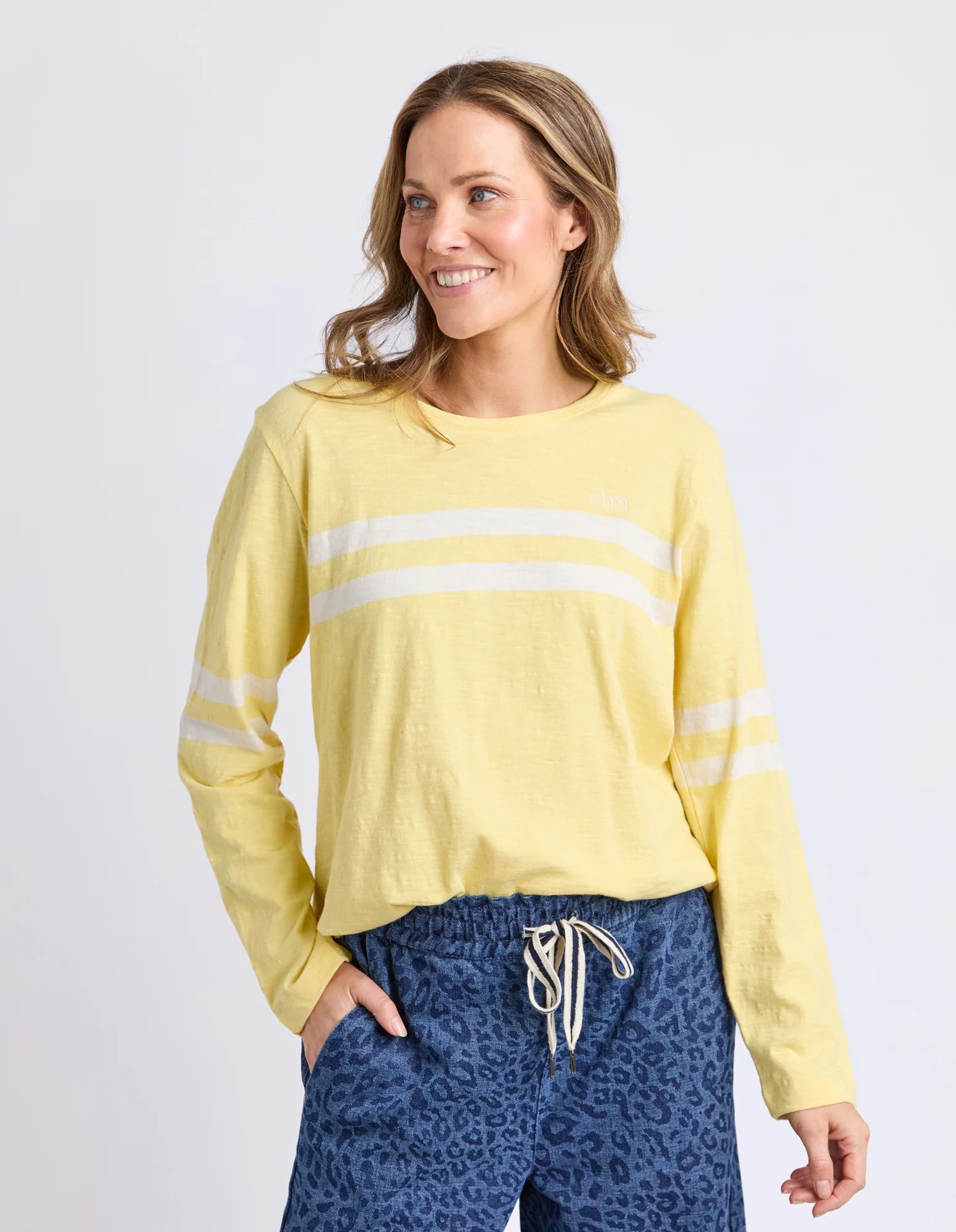 Image of Woman wearing a Elm yellow long-sleeve top with white stripes and blue leopard print pants on a light gray background