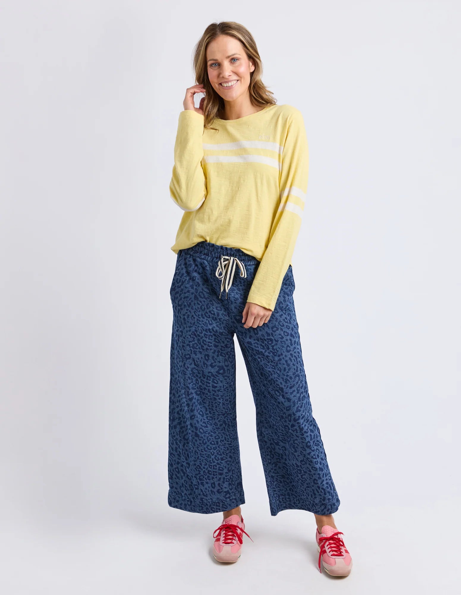 Woman wearing a Elm yellow long-sleeve top and blue patterned pants on a white background