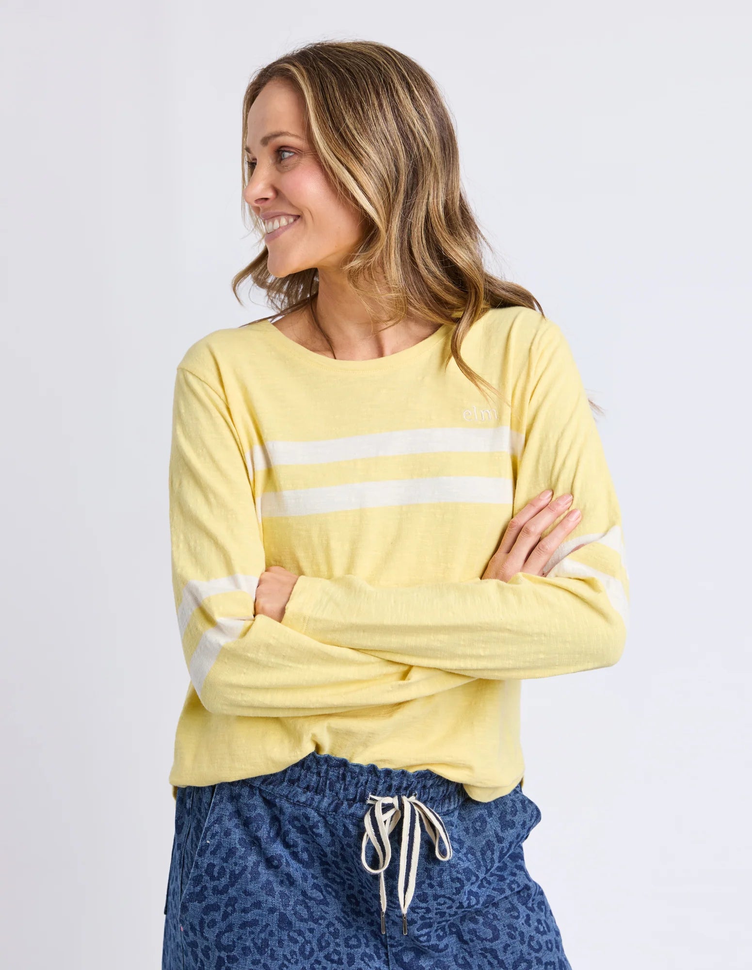 Woman wearing a Elm yellow long-sleeve top with white stripes on a plain background
