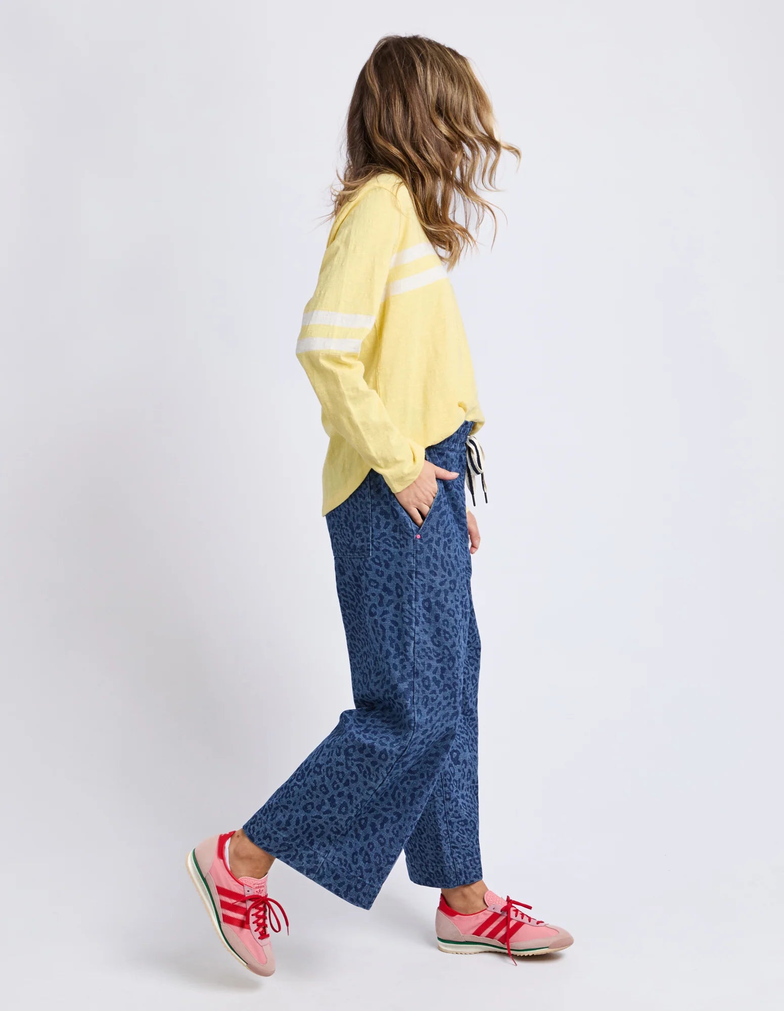 Woman wearing a Elm yellow top and blue patterned pants on a white background