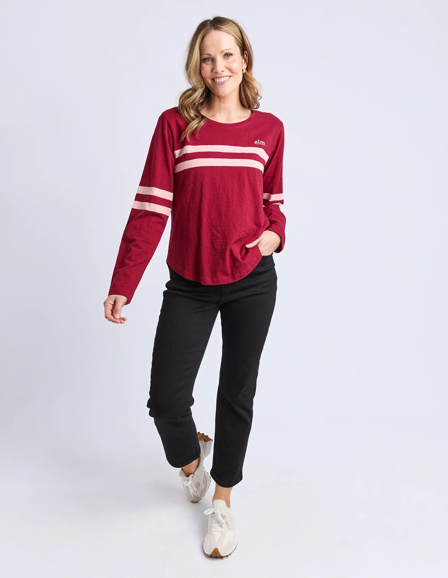 Image of Woman wearing a Elm red long-sleeve shirt with white stripes and black pants on a light gray background