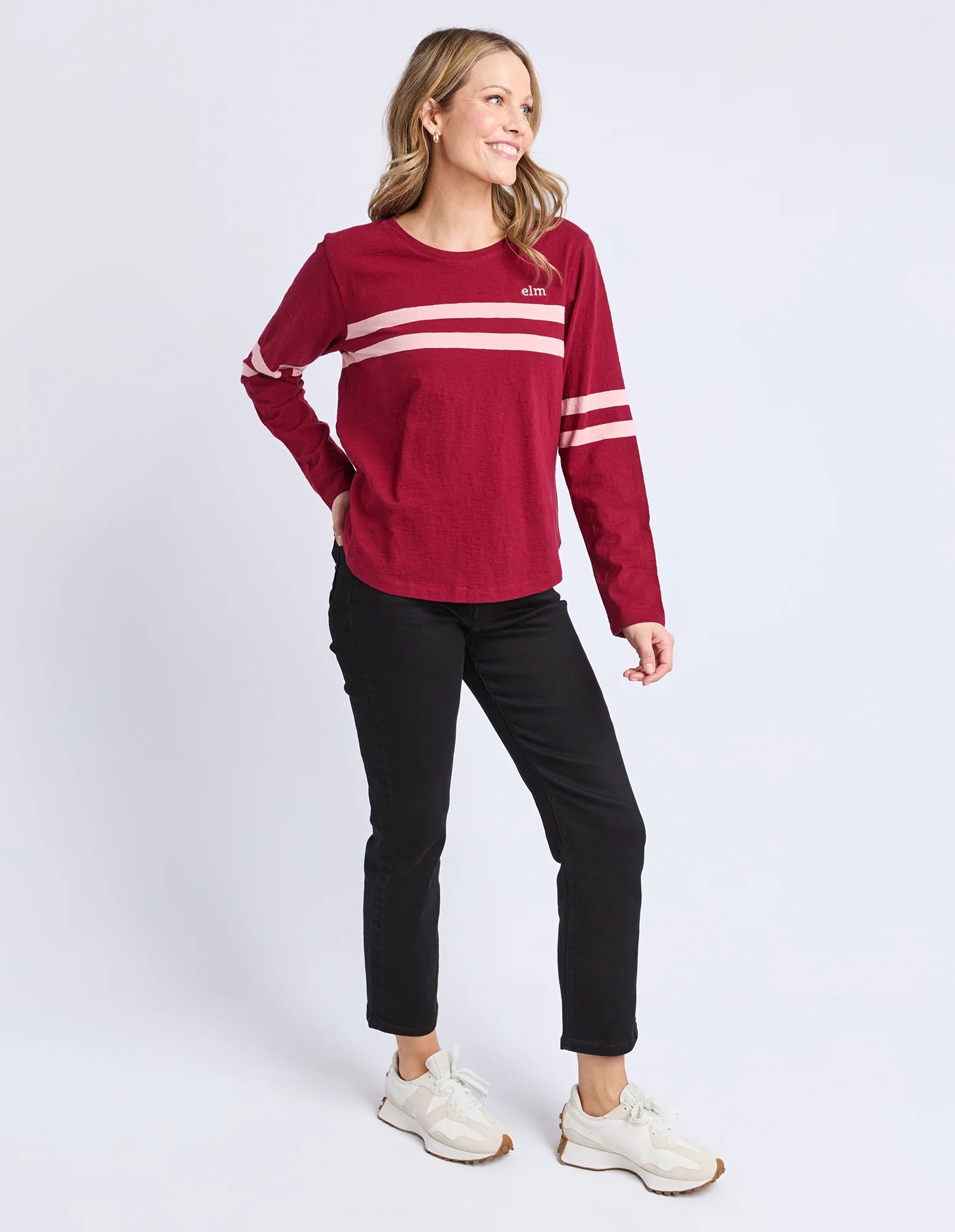Image of Woman wearing a Elm red long-sleeve shirt with white stripes and black pants on a white background