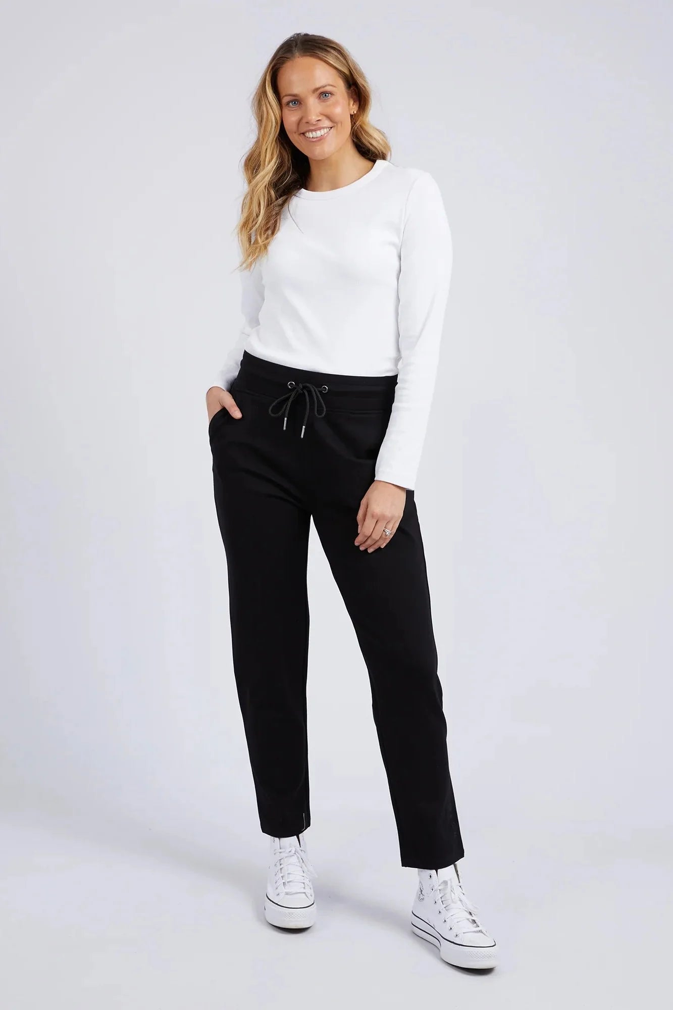 Image of Woman wearing a white sweater and Elm black pants on a white background