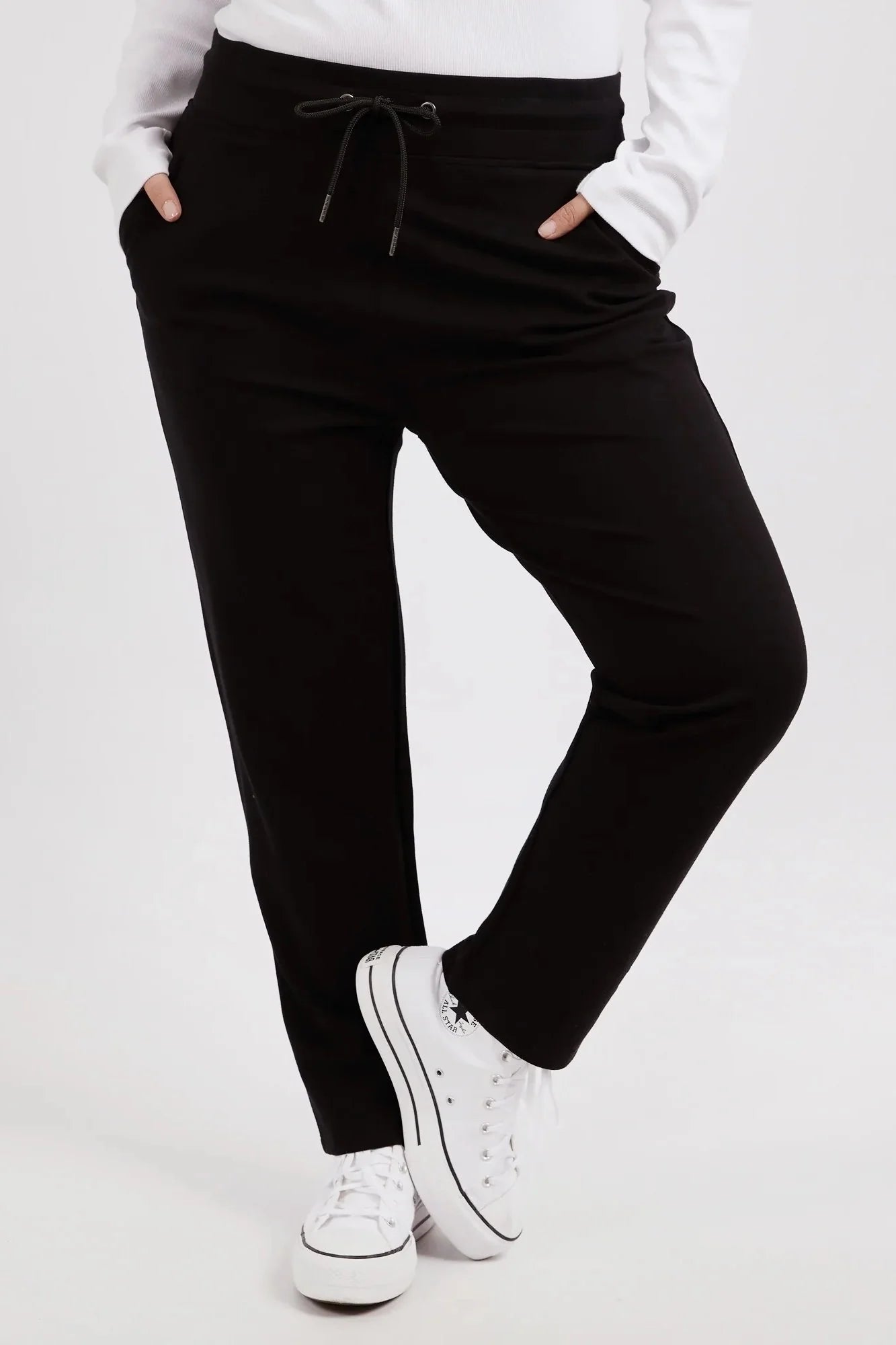 Image of Woman wearing Elm black jogger pants and white sneakers on a white background