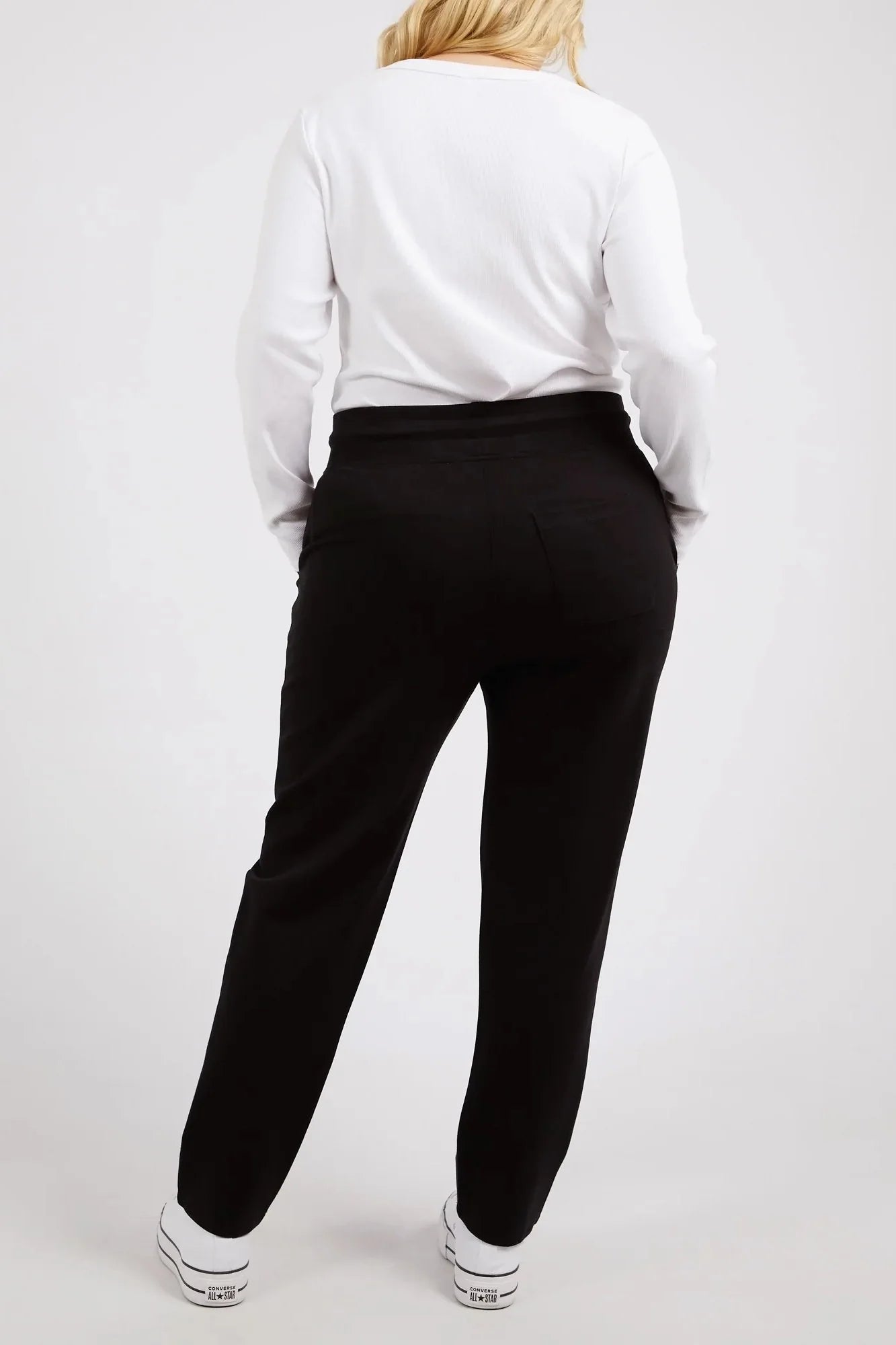 Image of Woman wearing a white shirt and Elm black pants on a plain background